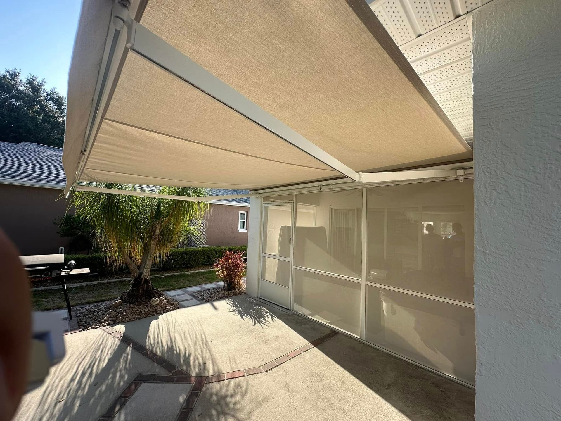 Covered patio with beige awning, concrete floor, and sliding glass doors beside a courtyard.