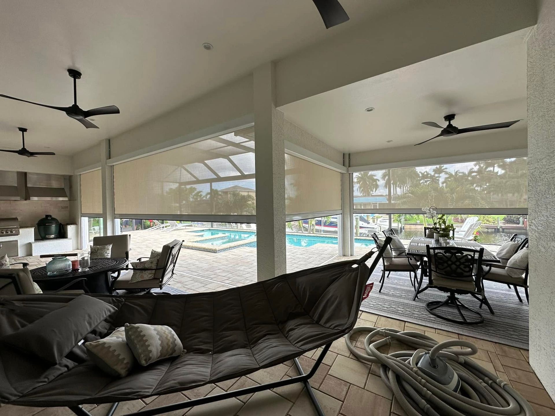 Covered patio lounge with sofas, chairs, ceiling fans, and a pool view beyond screened openings