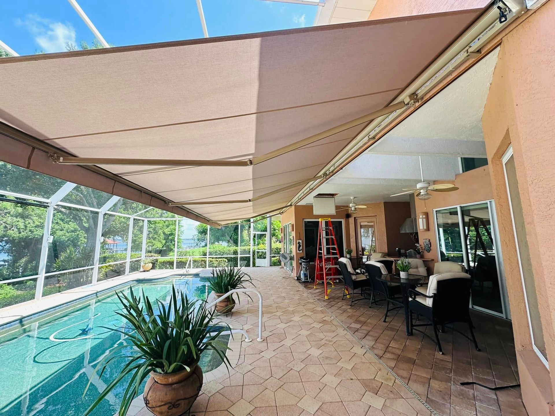 Covered patio with pool, potted plants, and outdoor dining seating beside large windows