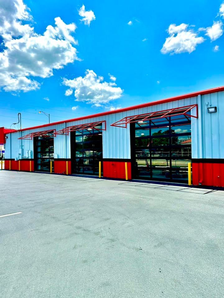 Red and white industrial building with glass garage doors under a bright blue sky with clouds