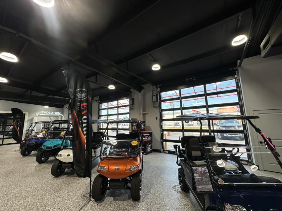 Golf carts displayed in a showroom with large glass garage doors and industrial lighting