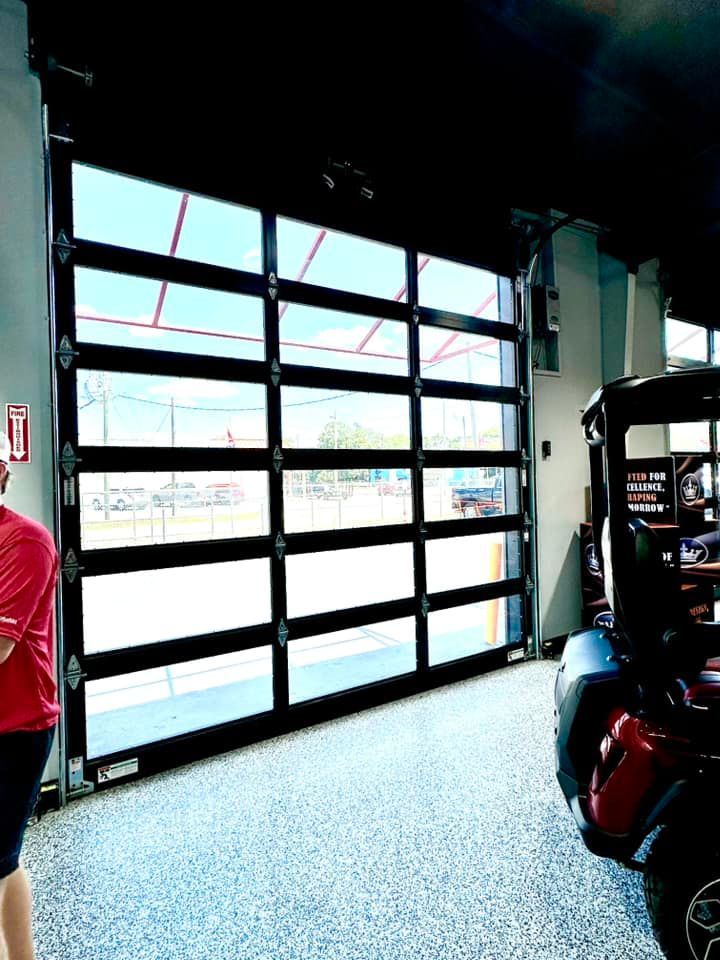 Bright garage interior with an open glass roll-up door and a red scooter parked inside.