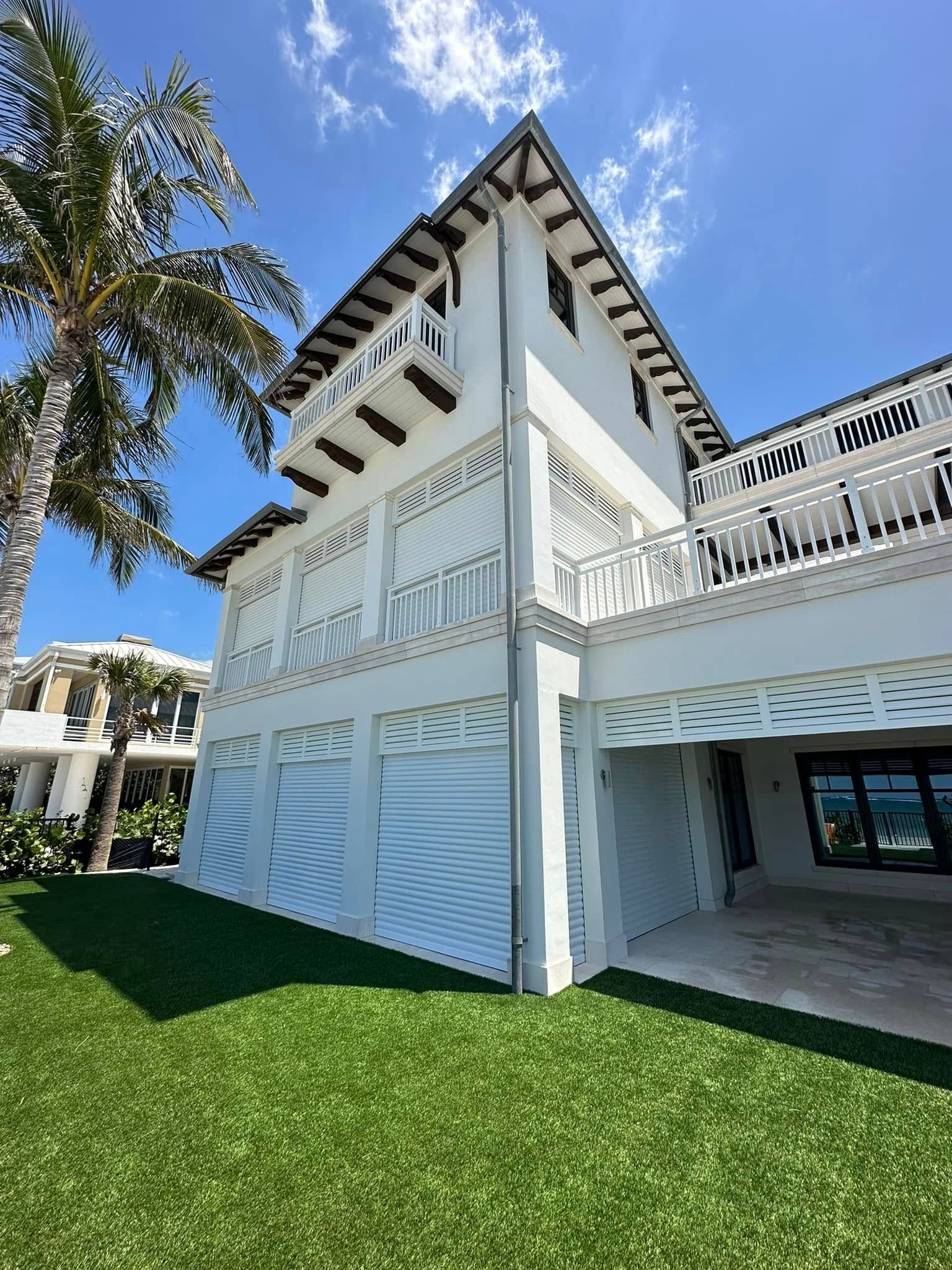 White tropical house with balconies and palm tree under a blue sky, beside a green lawn