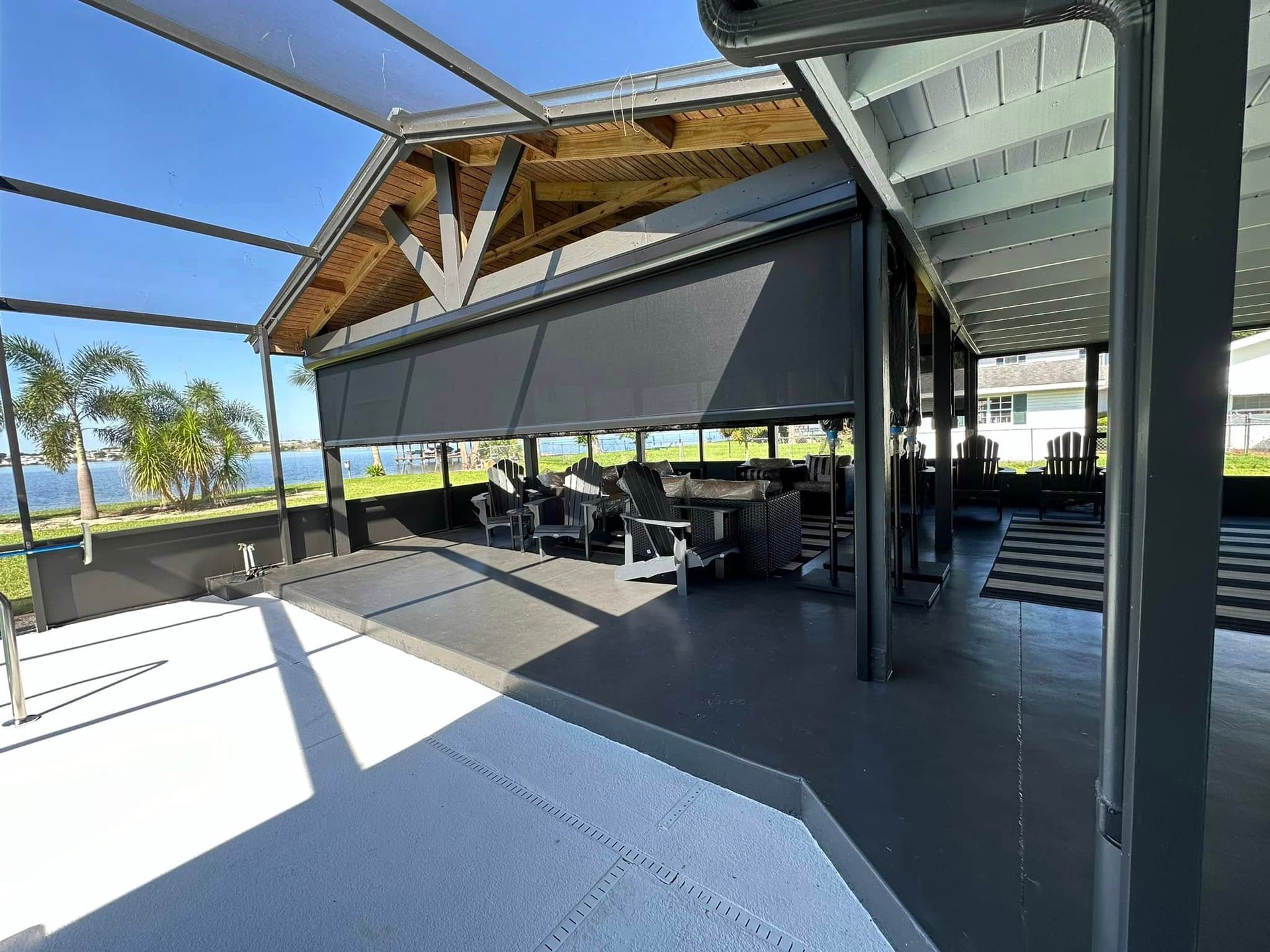 Covered outdoor patio with black retractable awnings, picnic tables, and ocean view beyond the railing