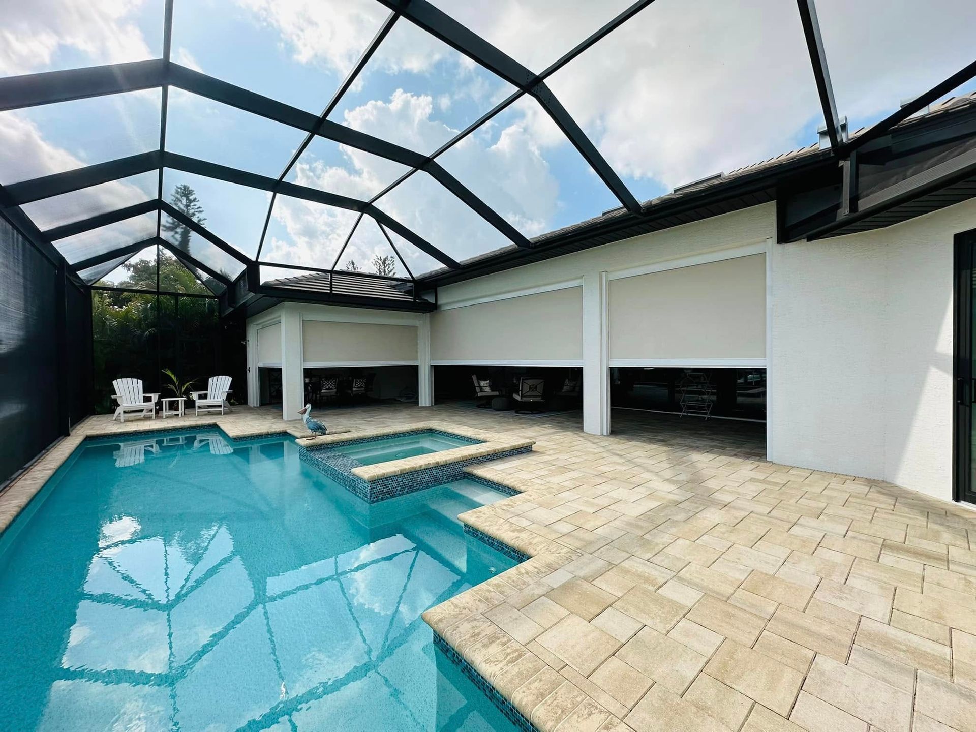 Covered backyard pool with blue water, beige paver deck, and white patio seating under a screened enclosure