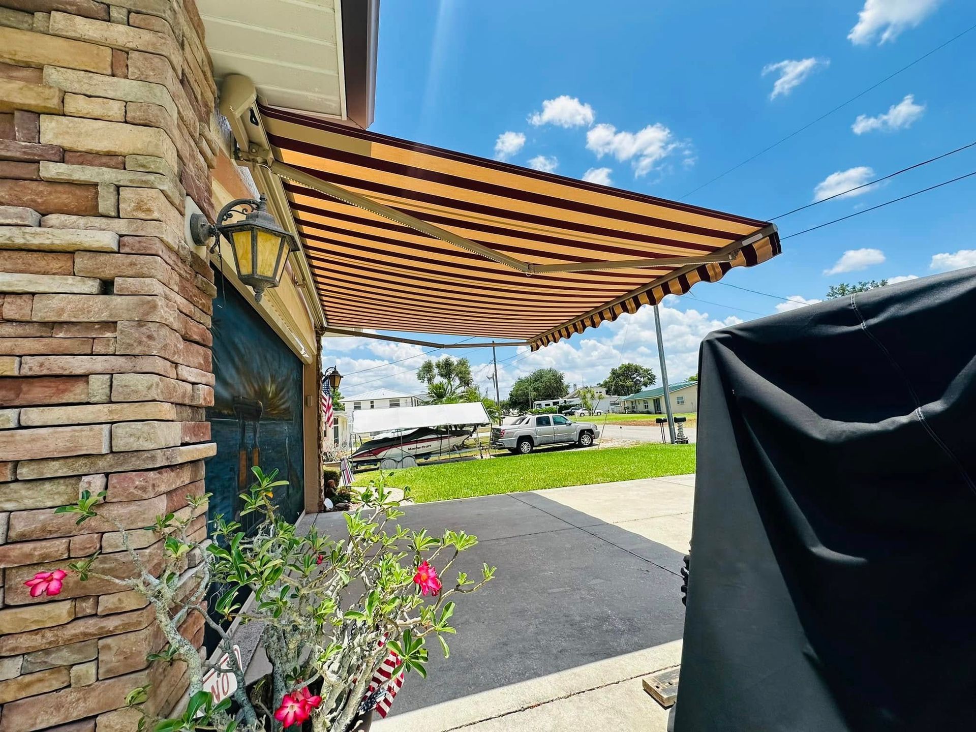 Brick building entrance with striped awning, potted flowers, and driveway under a blue sky
