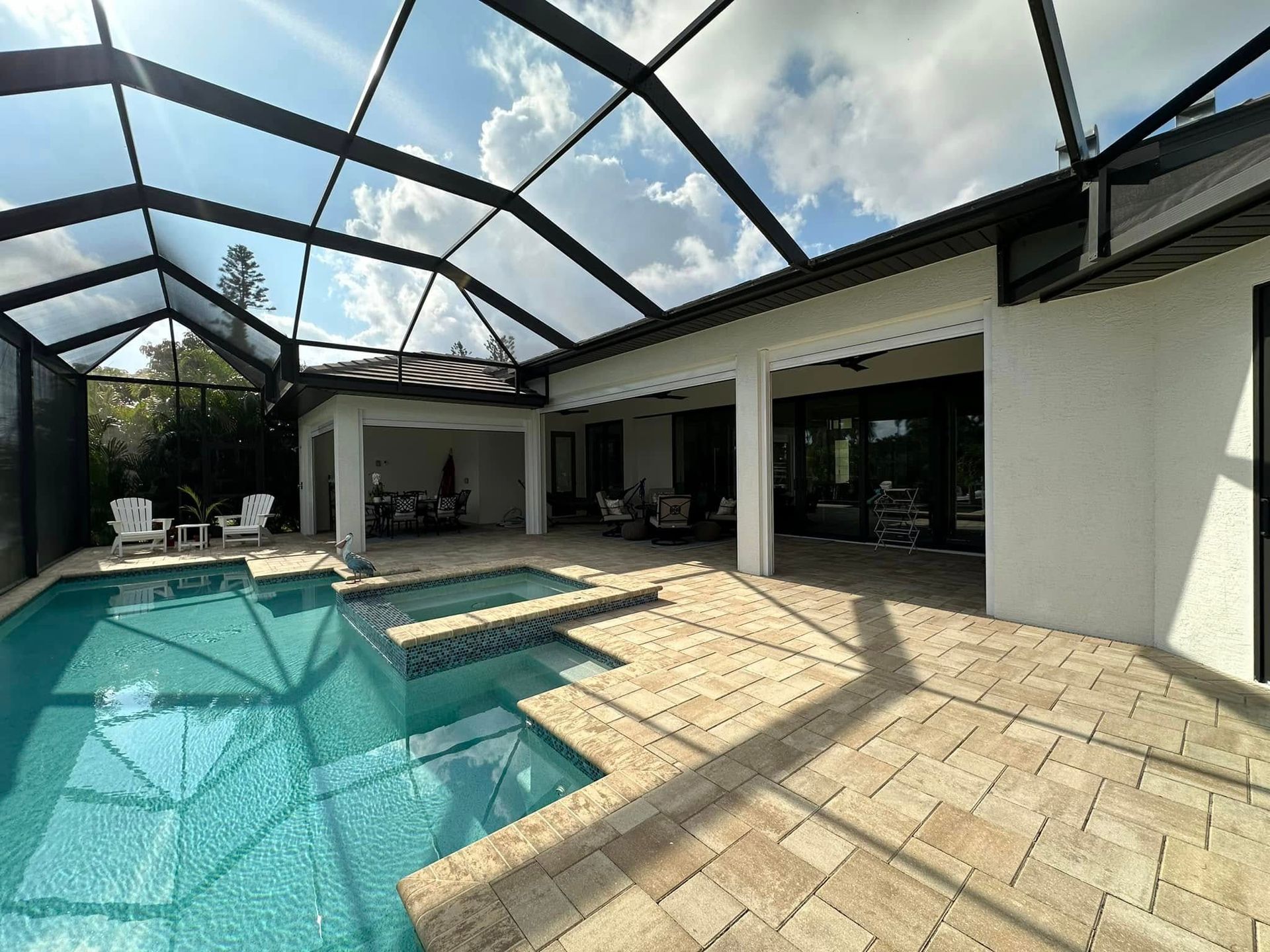 Screened-in patio with a turquoise pool, stone pavers, and a covered seating area under a black frame roof