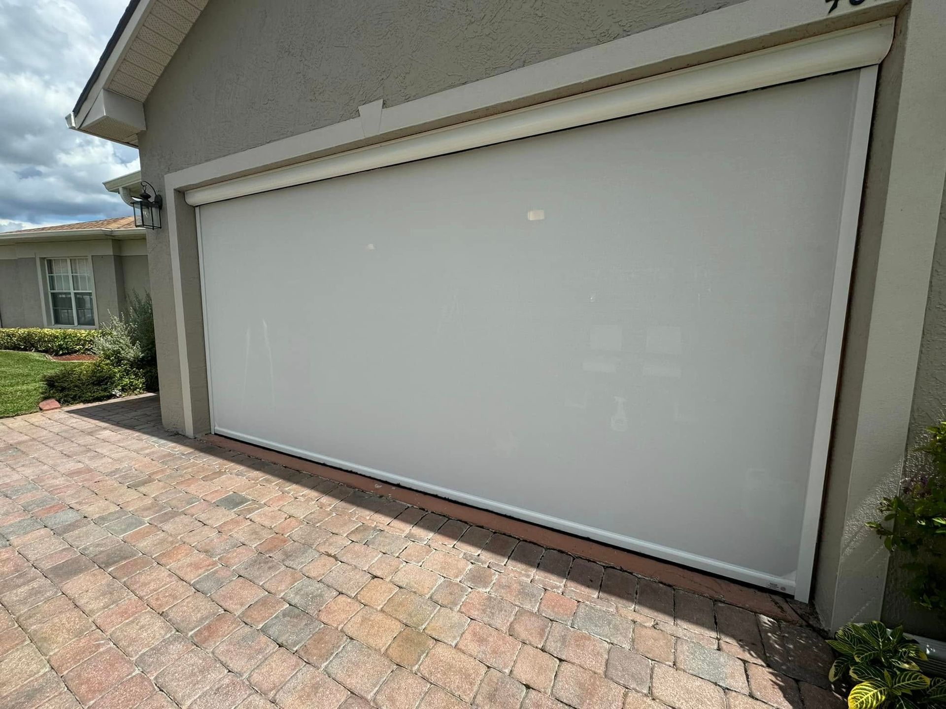 Closed white garage door on a house with a brick driveway and gray exterior walls