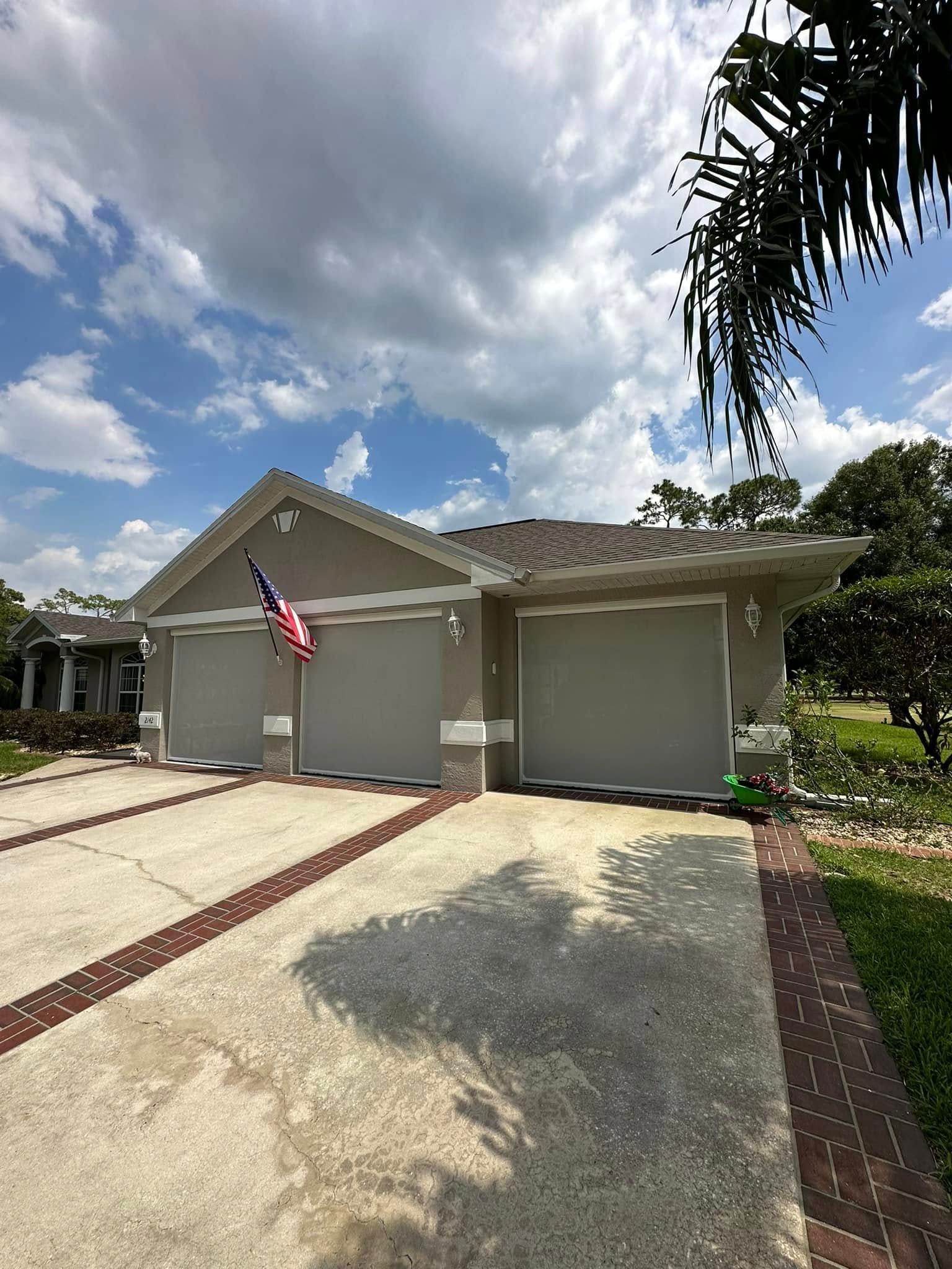 Single-story suburban house with a two-car garage, American flag, and cloudy sky.
