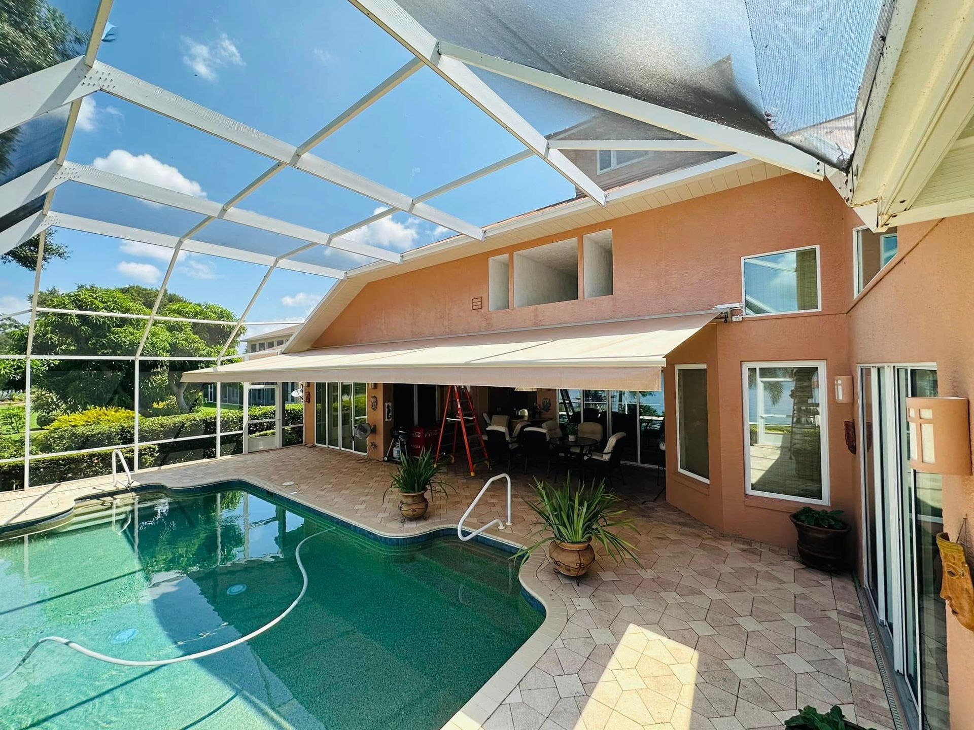 Screened backyard pool with patio, white awning, and peach house under a glass enclosure