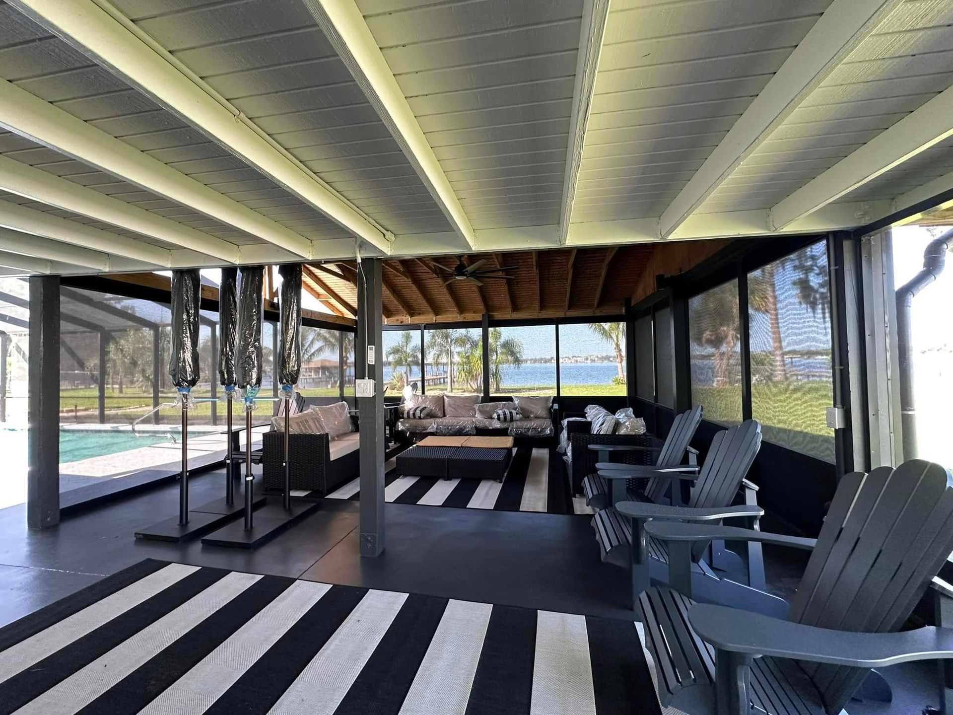 Covered patio with black-and-white striped floor, chairs, and a view of the pool and yard beyond.
