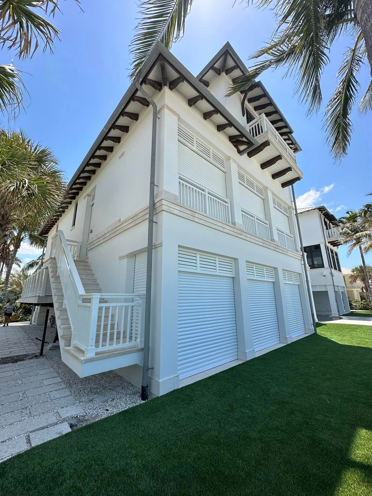 White beach house with exterior stairs, balconies, and a red-tiled roof under palm trees.