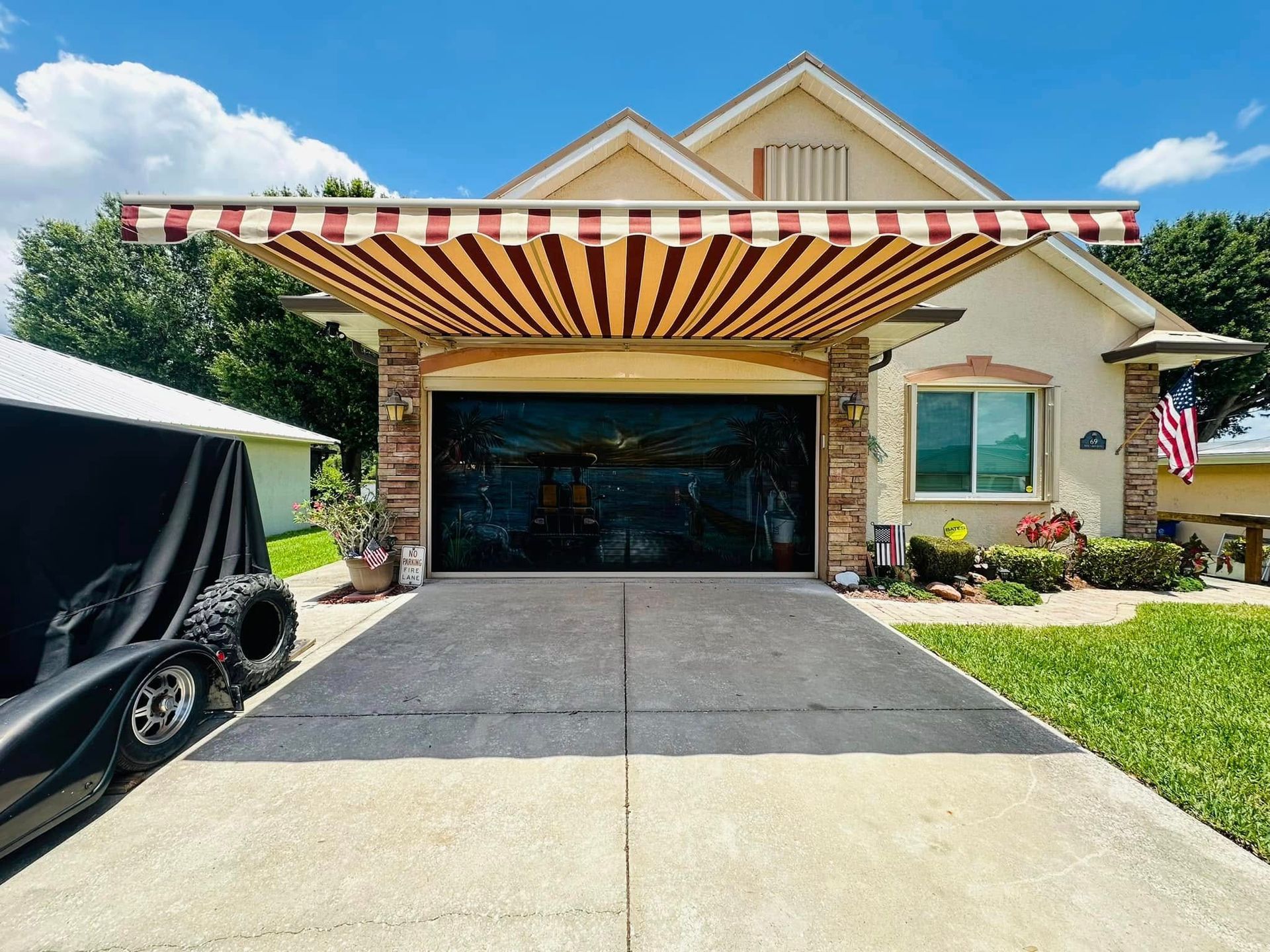 Suburban house with striped awning over a driveway and parked vehicle under a cloudy sky