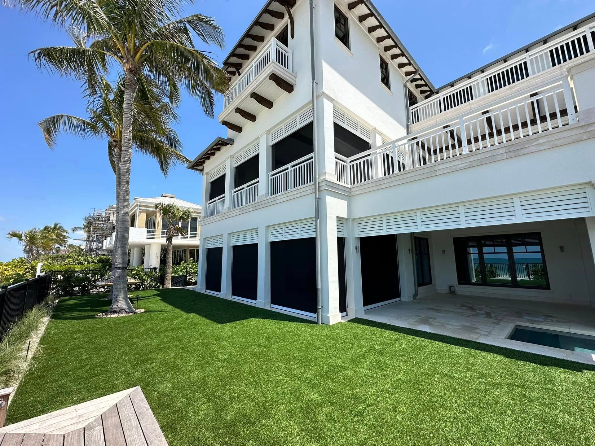 White coastal house with balconies, green lawn, palm tree, and blue sky