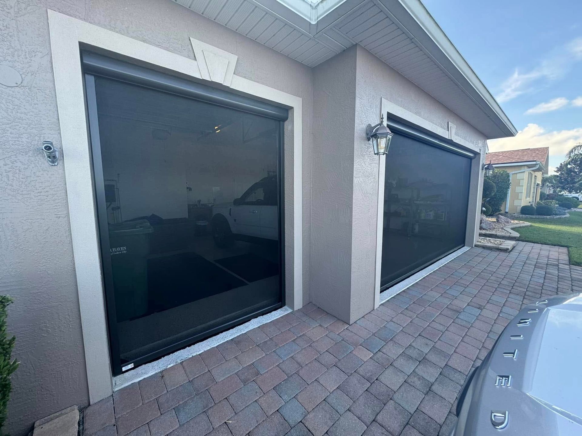 Modern house exterior with two dark tinted sliding doors and a tiled patio beside a driveway