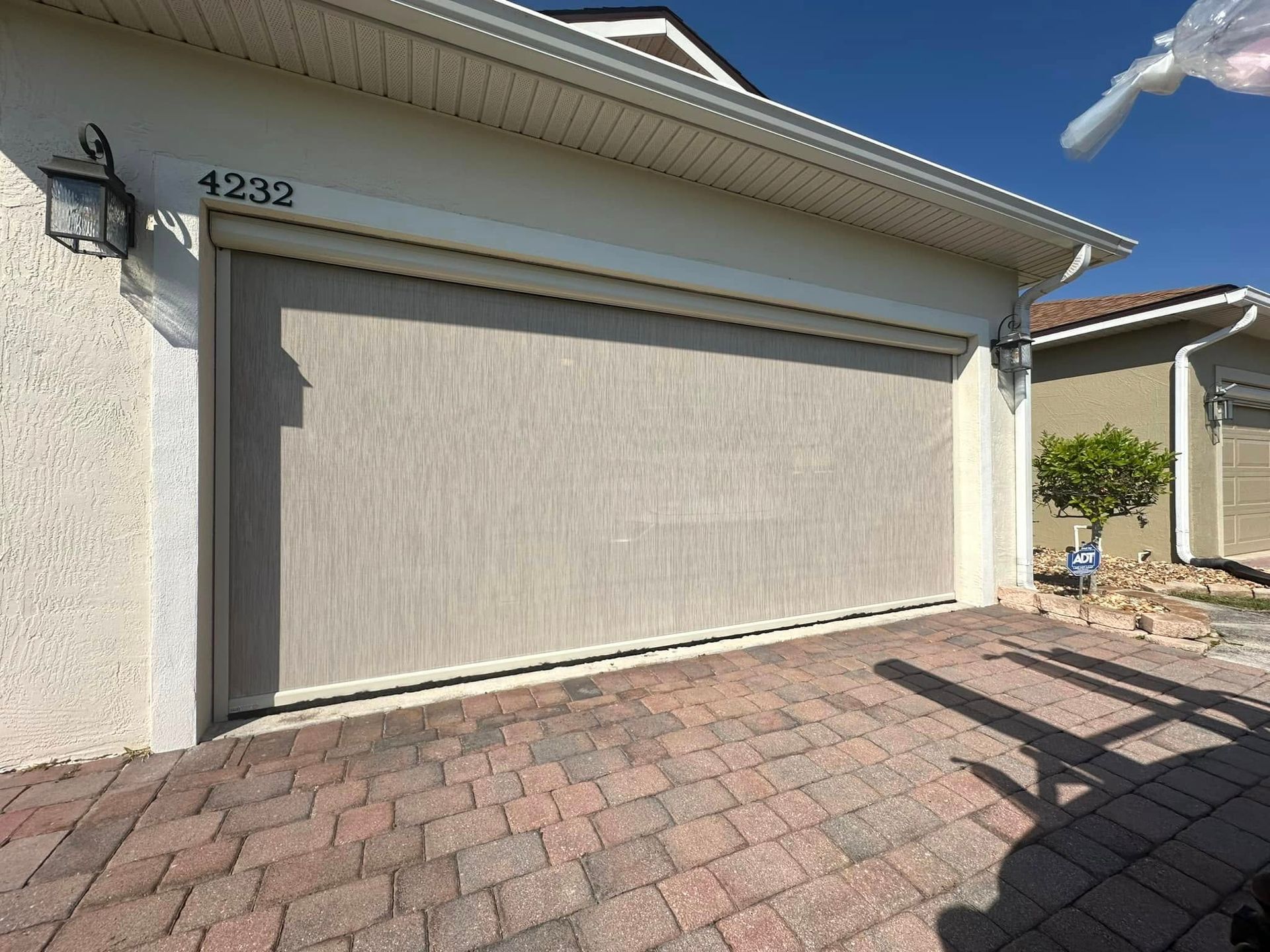 Closed beige garage door with house number 4232 and brick driveway in front