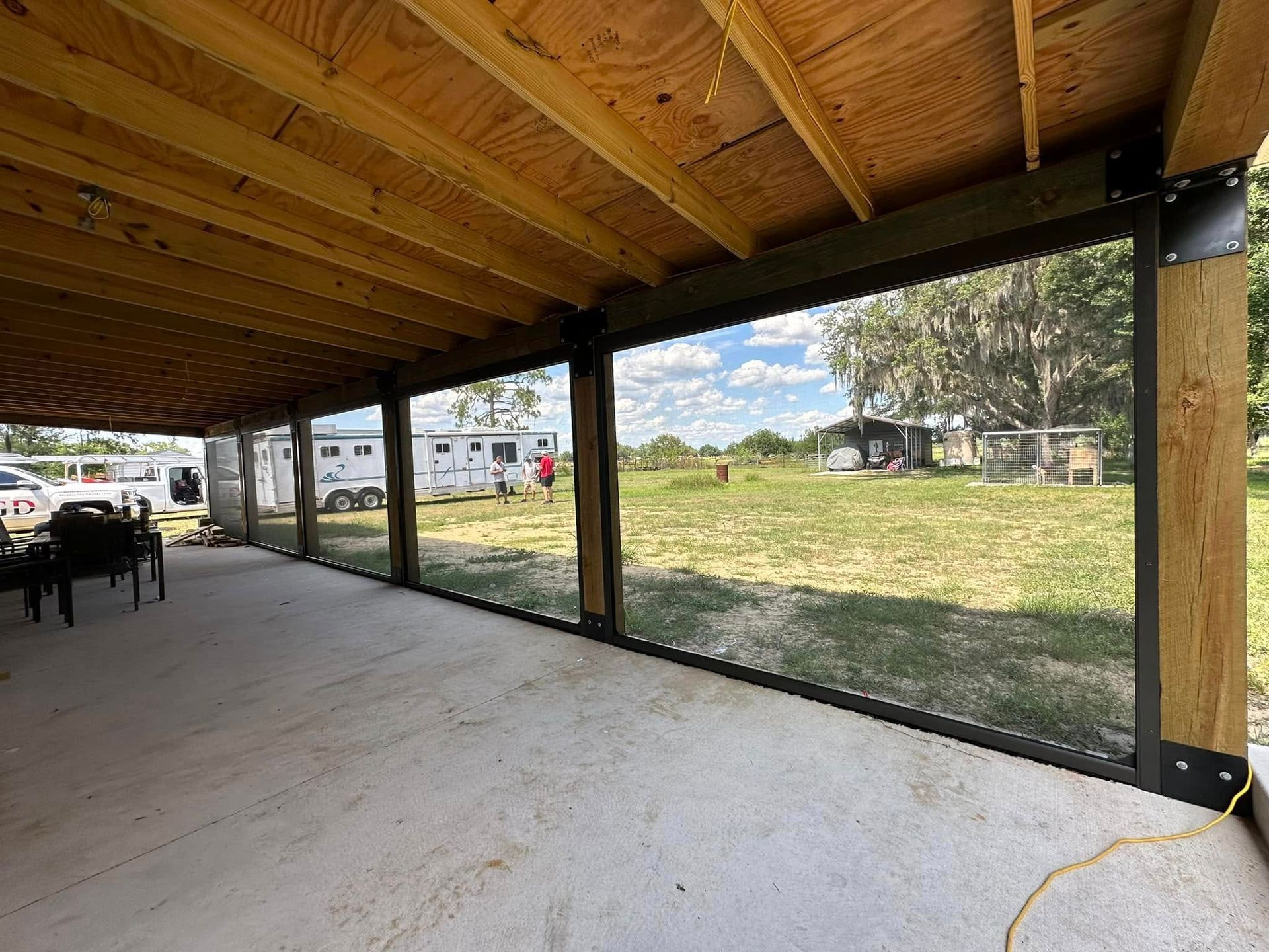 Covered outdoor patio with wooden roof, concrete floor, and grassy yard beyond open mesh panels