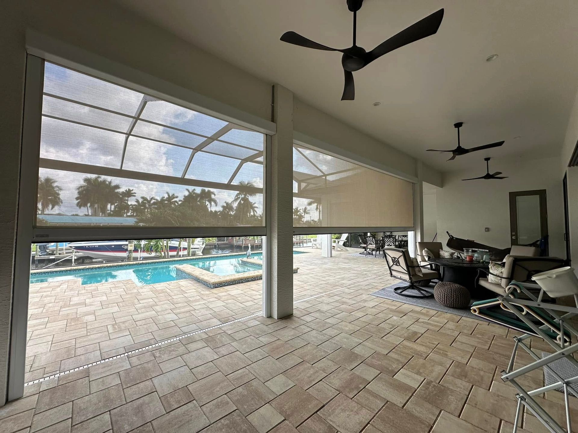 Covered patio with tile floor, ceiling fans, seating, and a pool view through open blinds