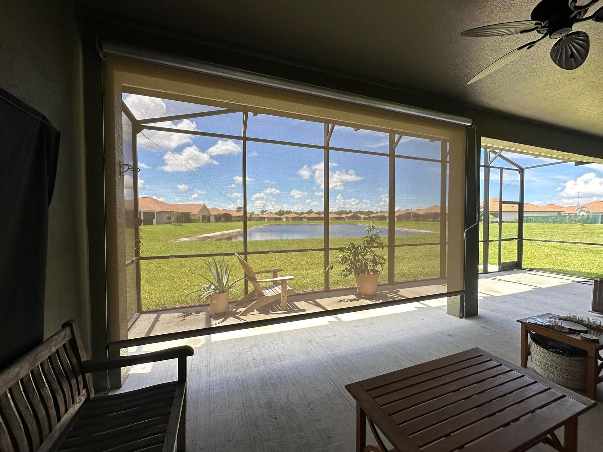Covered patio overlooking a sunny lake and green field, with wooden seating and a small table.