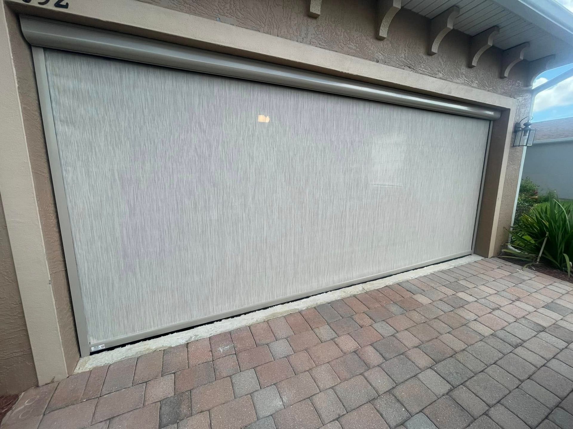 Closed white garage door with textured paneling beside a brick driveway and house exterior