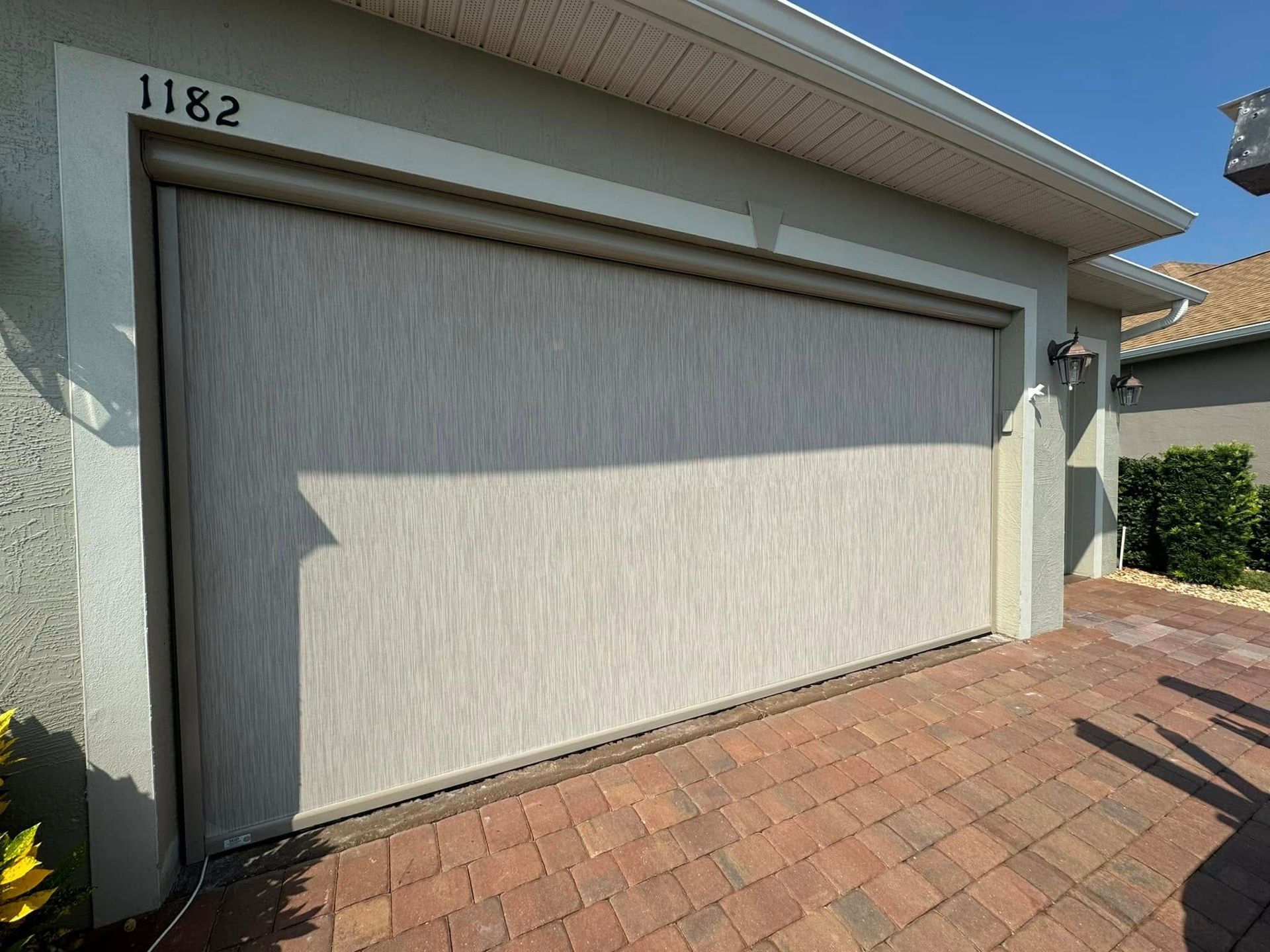 Closed cream-colored garage door on a house with a brick driveway and house number 1182.