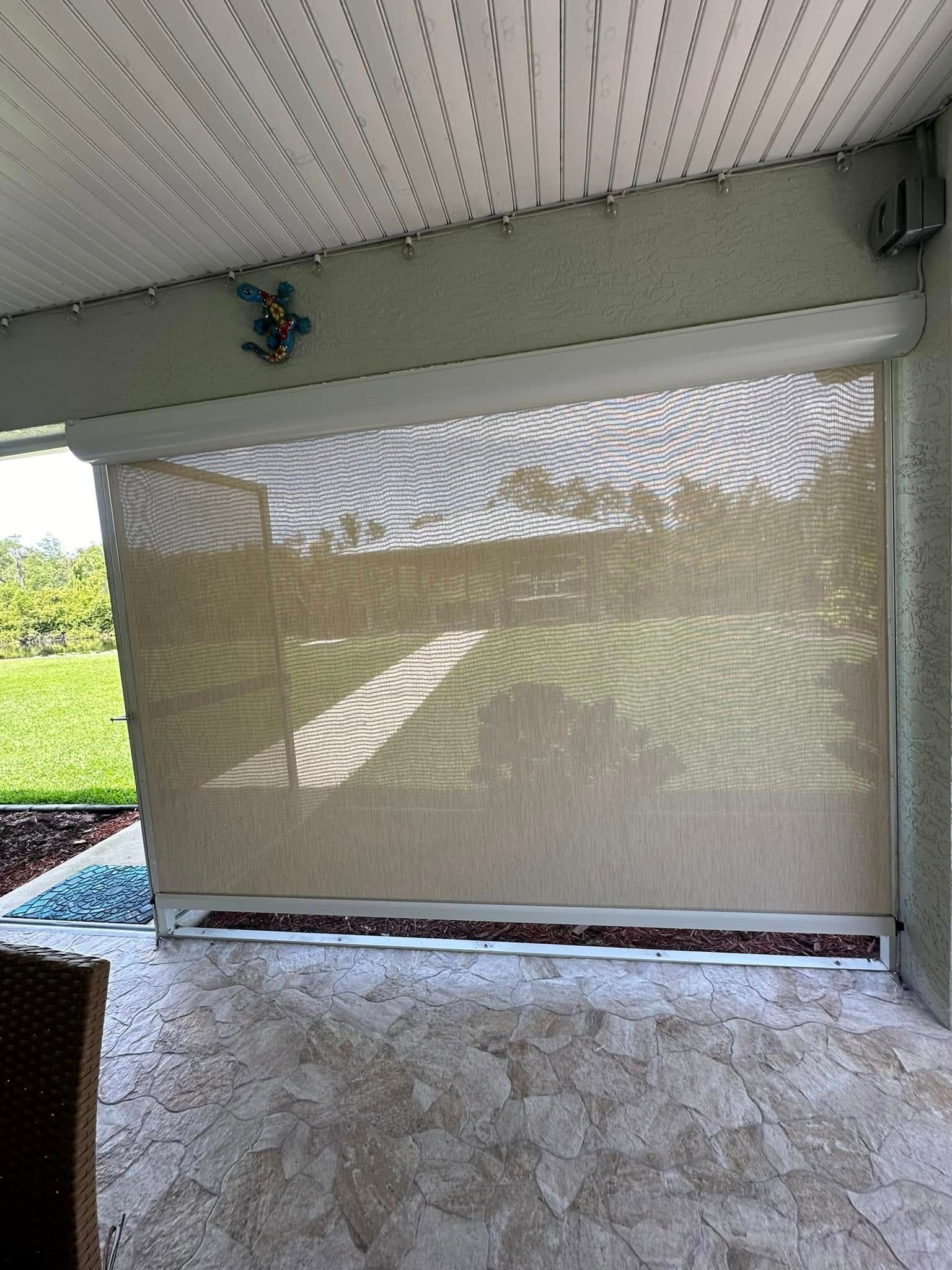 Outdoor patio with a beige sunshade blind, white ceiling, and grassy yard beyond