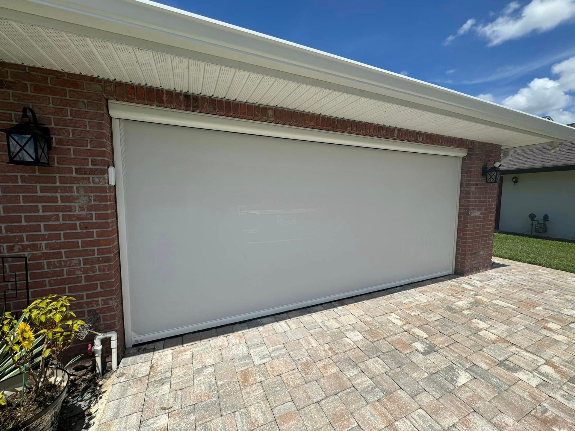 Closed white garage door on a brick house with a tiled driveway and blue sky above