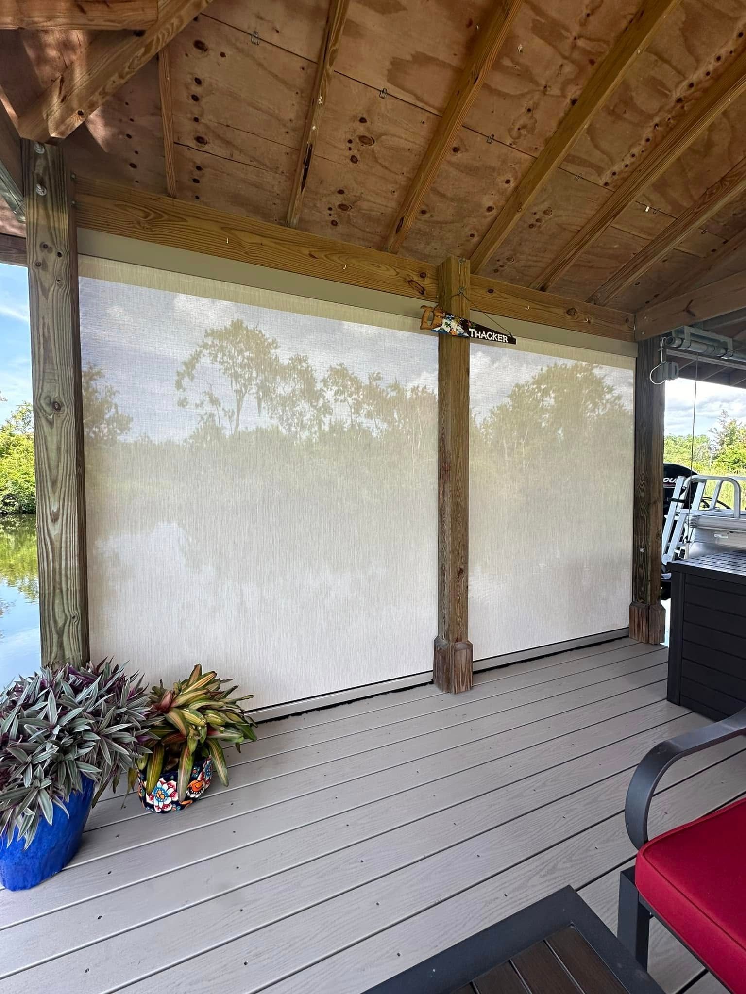 Covered porch with gray deck boards, wooden posts, potted plants, and a red chair in the corner