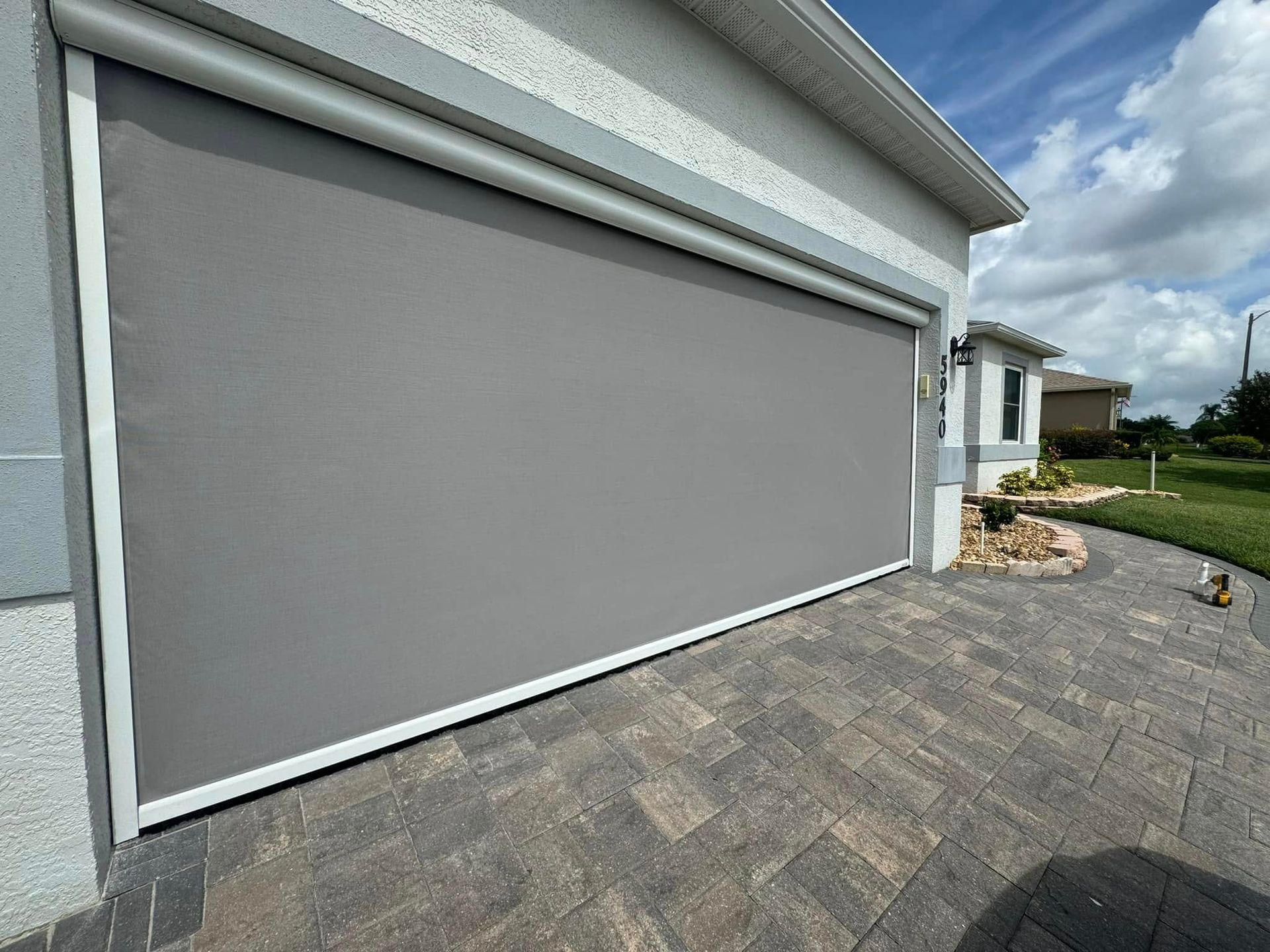 Closed gray garage door beside a paved driveway and lawn under a partly cloudy sky