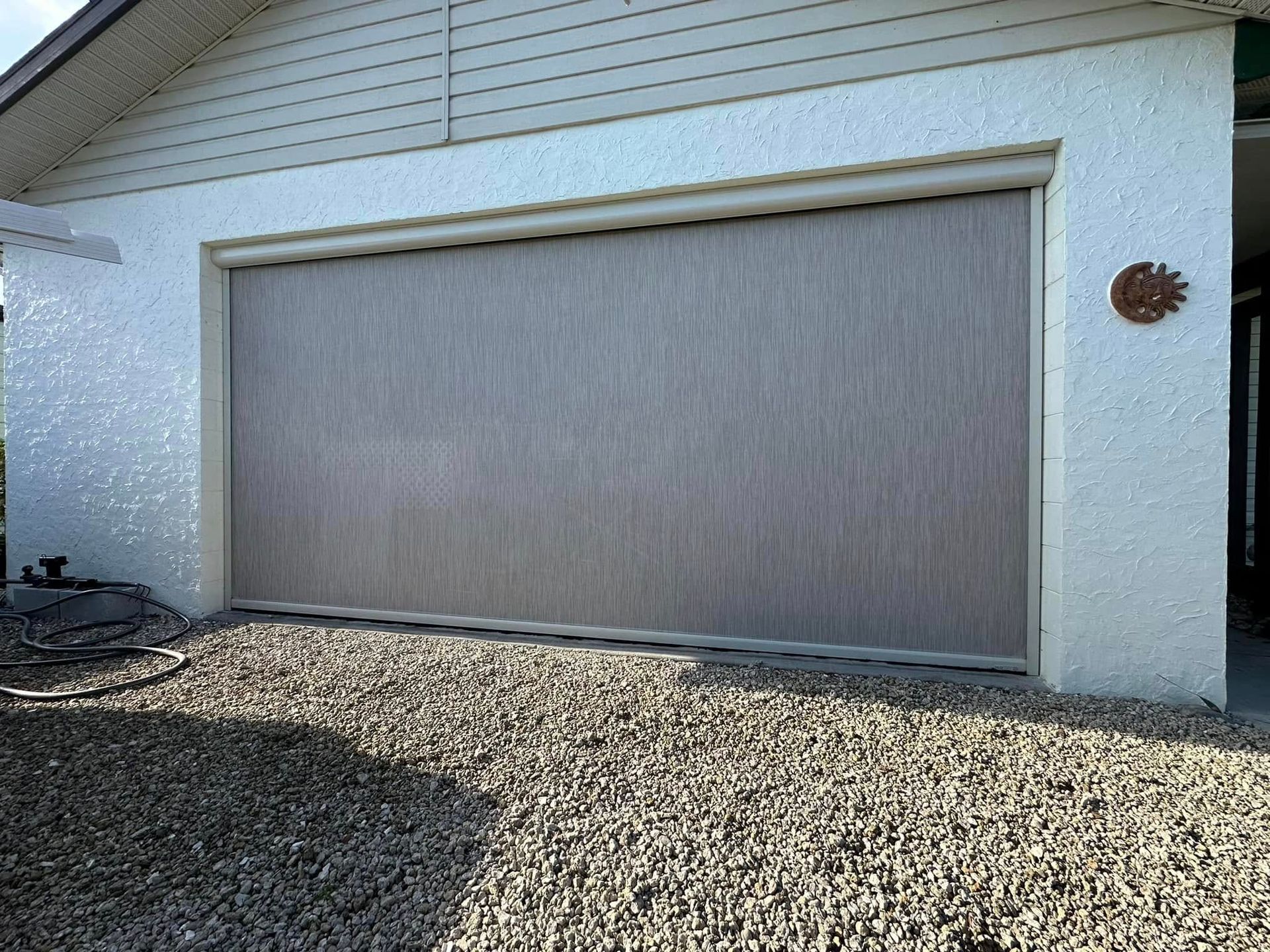 House with a closed gray garage door and gravel driveway under a white exterior wall