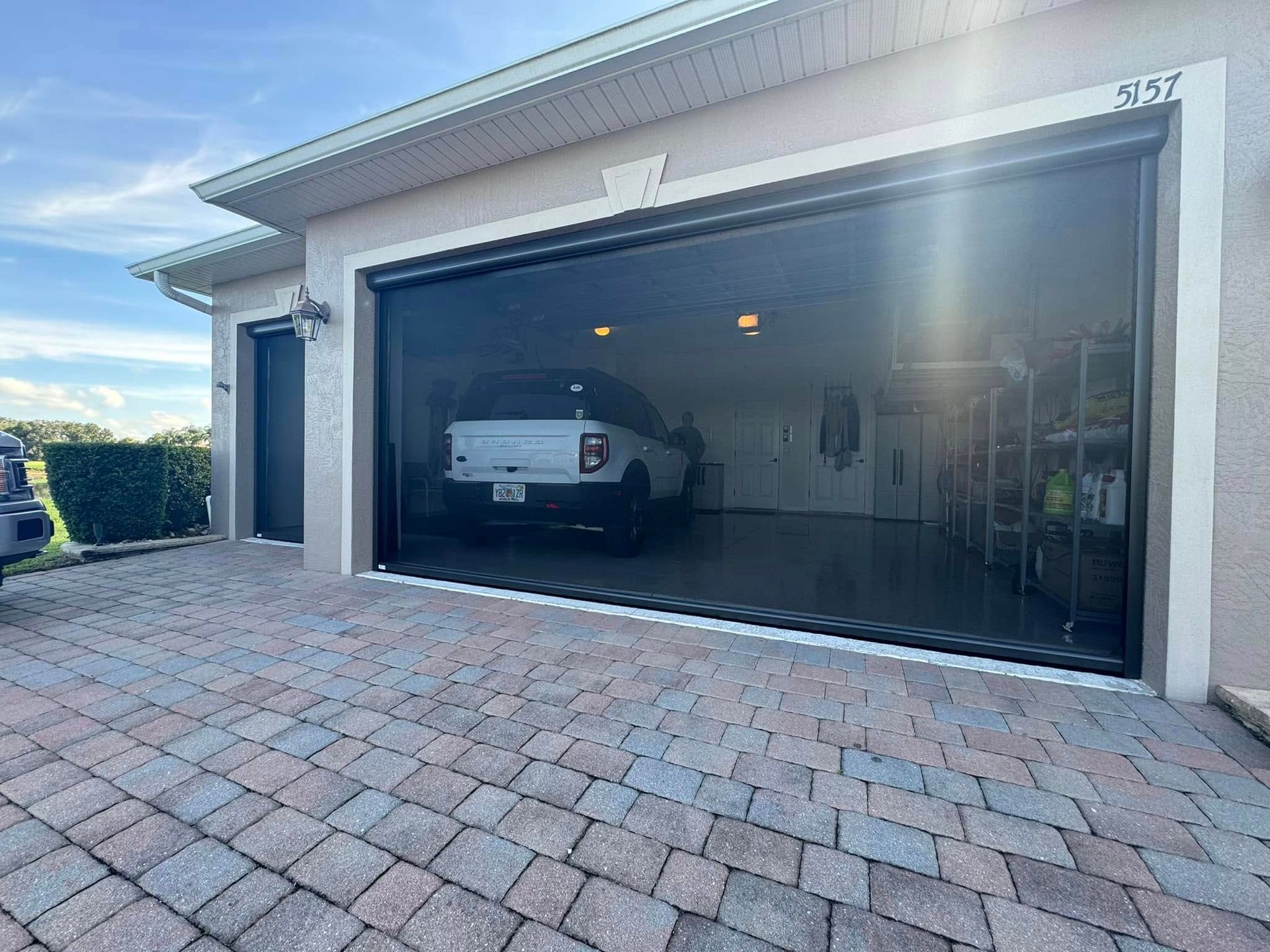 Open garage with a white car parked inside and brick-paved driveway in front