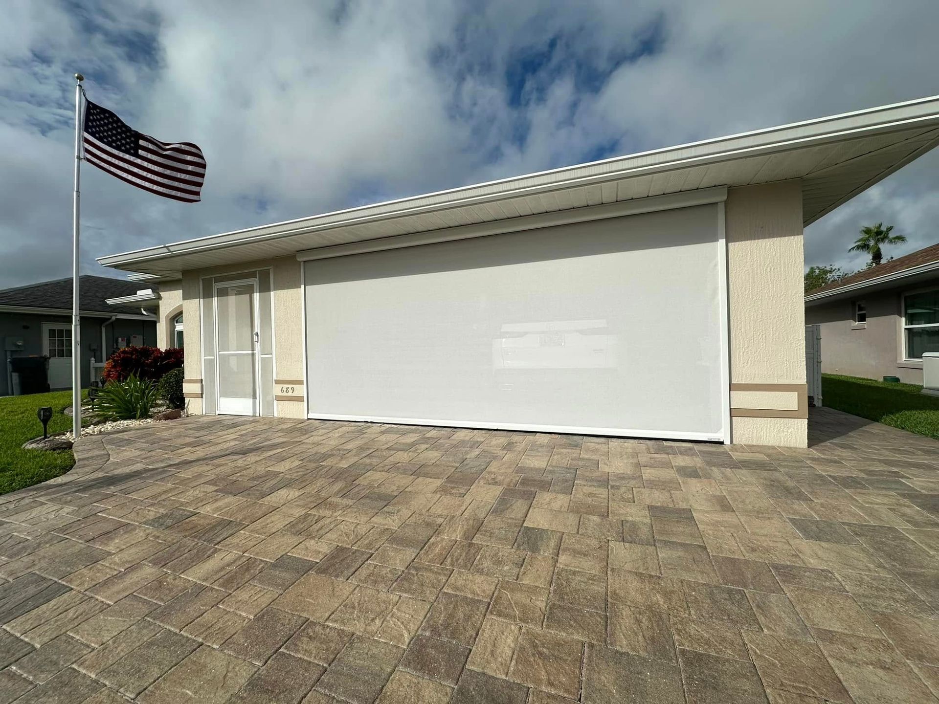 Modern single-story house with a white garage door, paver driveway, and an American flag outside