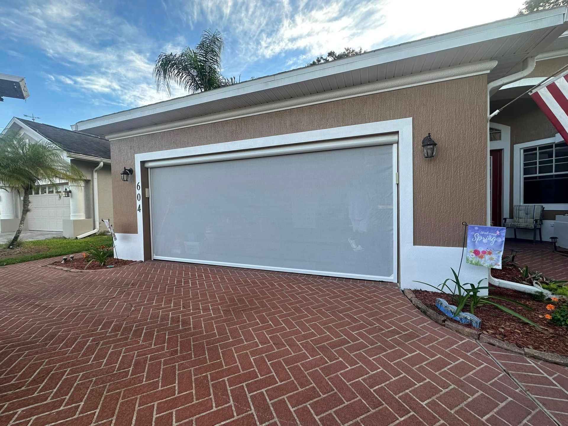 Suburban brick driveway and two-car garage with a closed gray door under a partly cloudy sky
