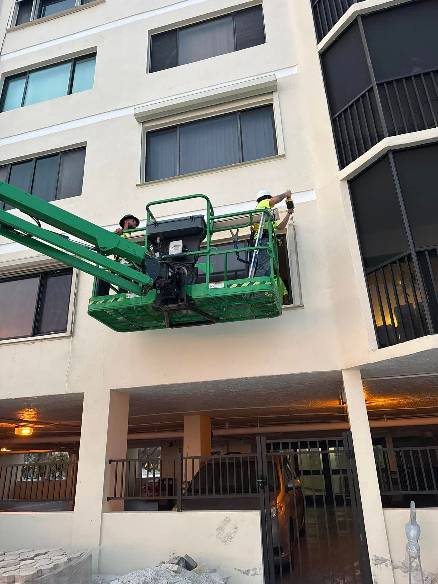 Green boom lift raised outside a beige apartment building, reaching a worker near upper windows