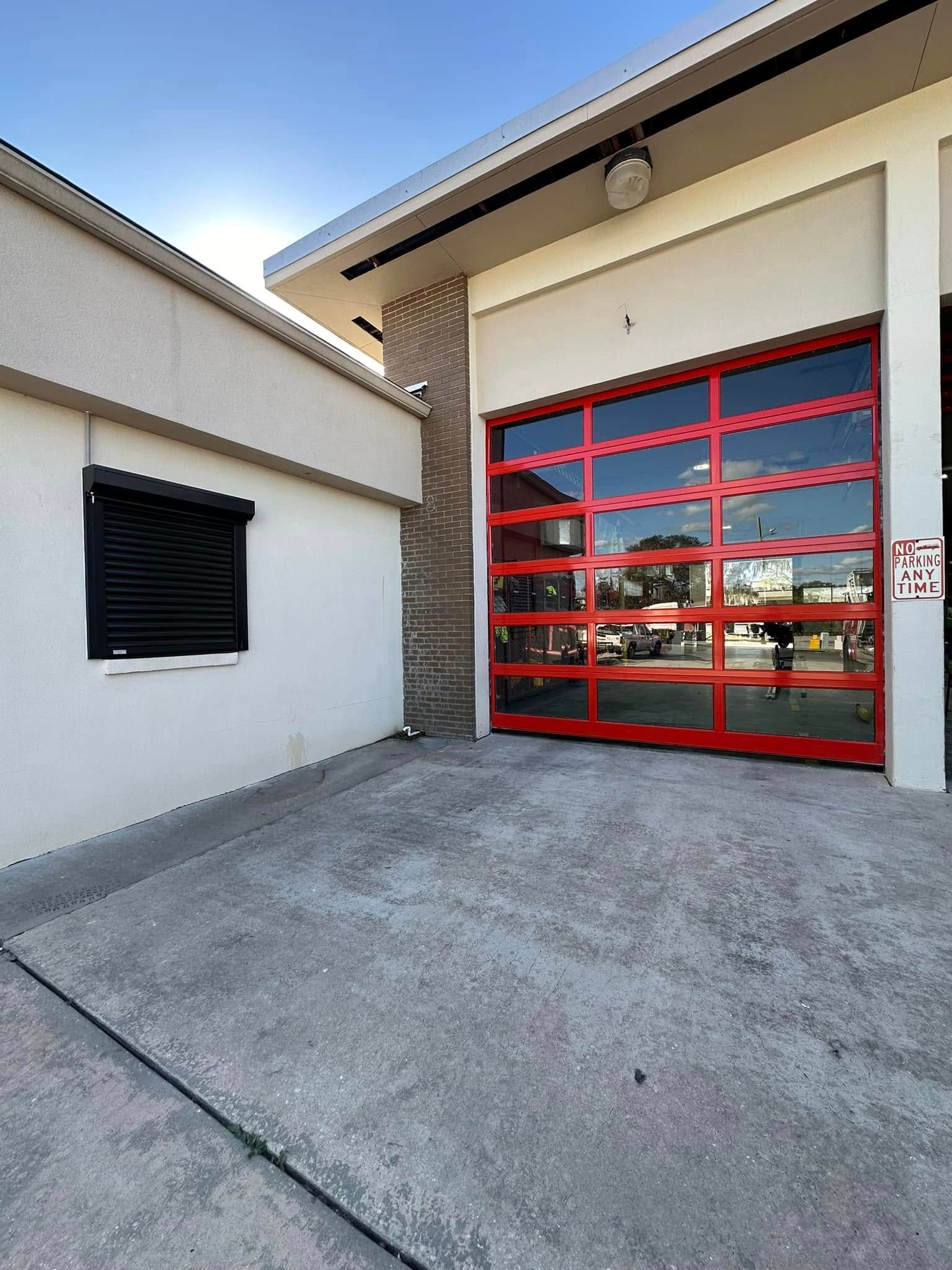 Red-framed glass garage door beside a white building and concrete driveway, viewed from outside