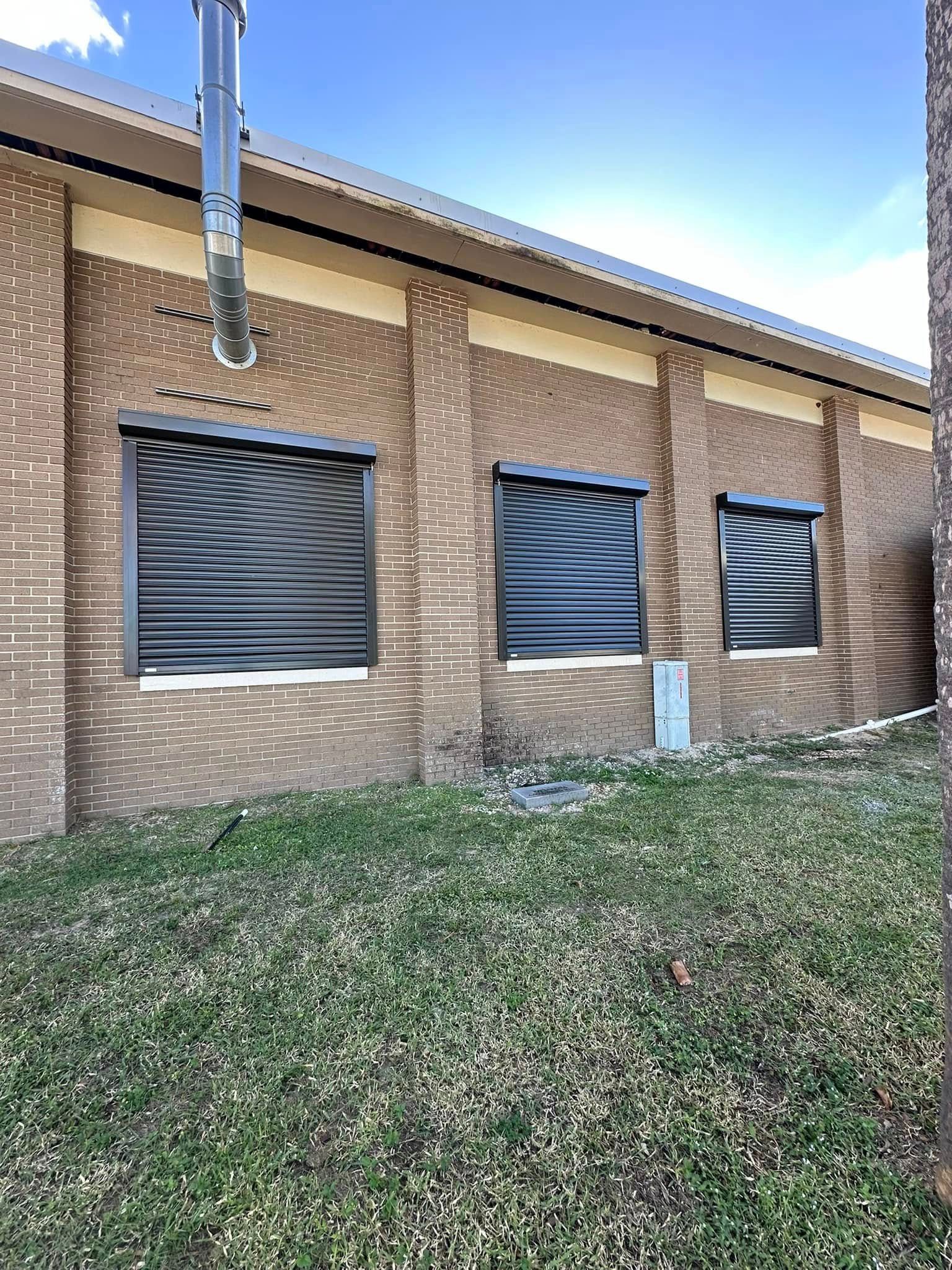 Brick building exterior with three windows and a grassy slope in front under a blue sky