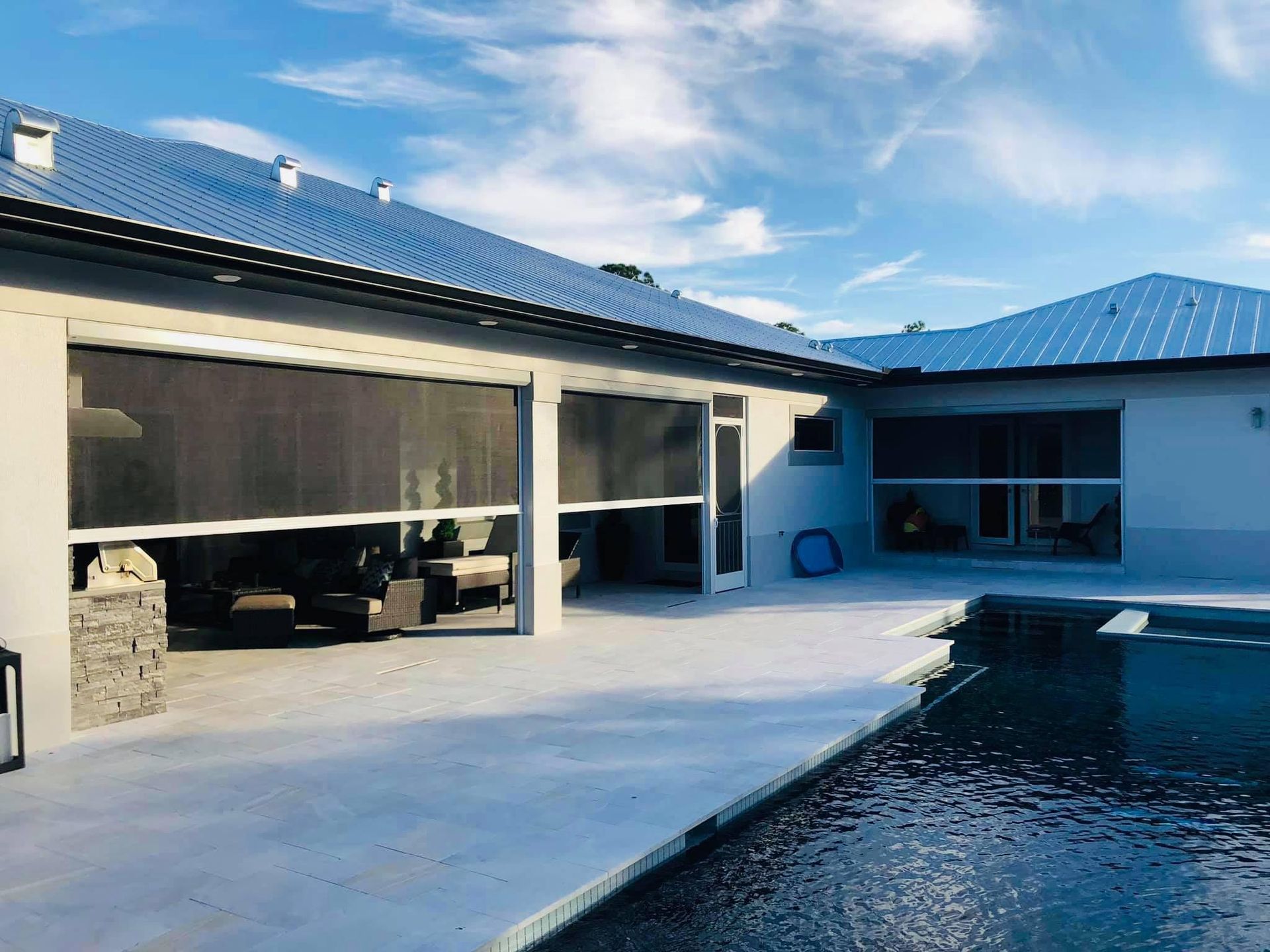 Modern house patio with blue-tiled pool and open covered seating area under a cloudy sky