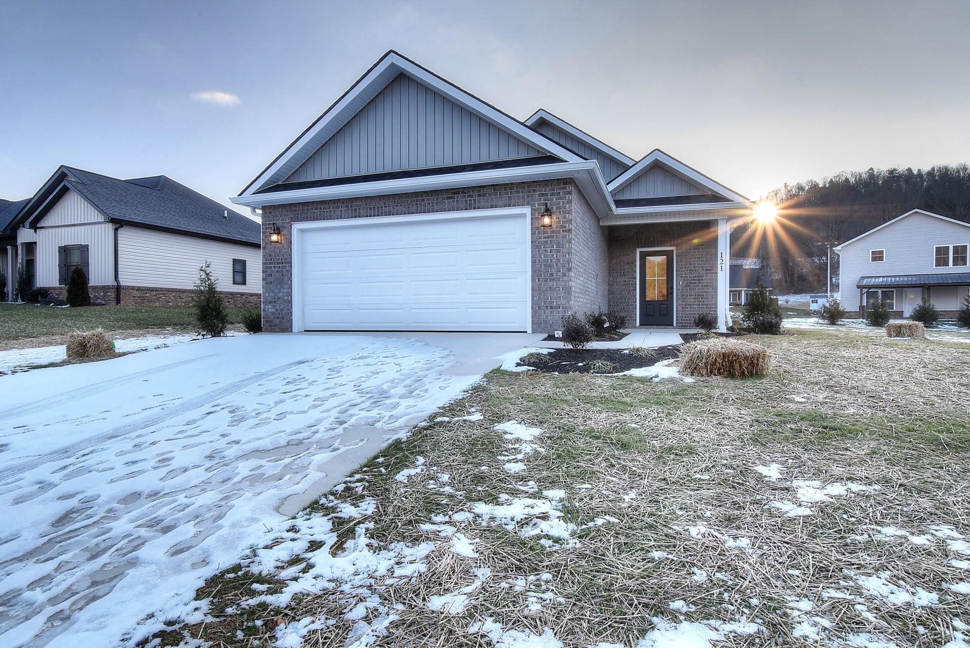 Snowy suburban house with a two-car garage at sunrise, front yard lightly covered in snow.