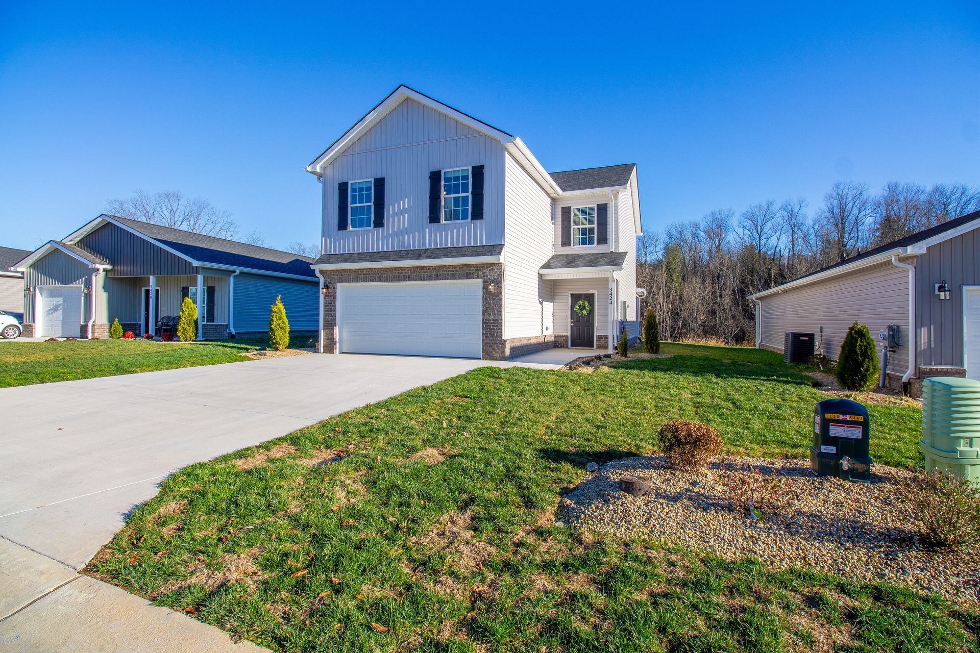 Two-story suburban house with white siding, blue shutters, a driveway, and a front lawn under a clear blue sky