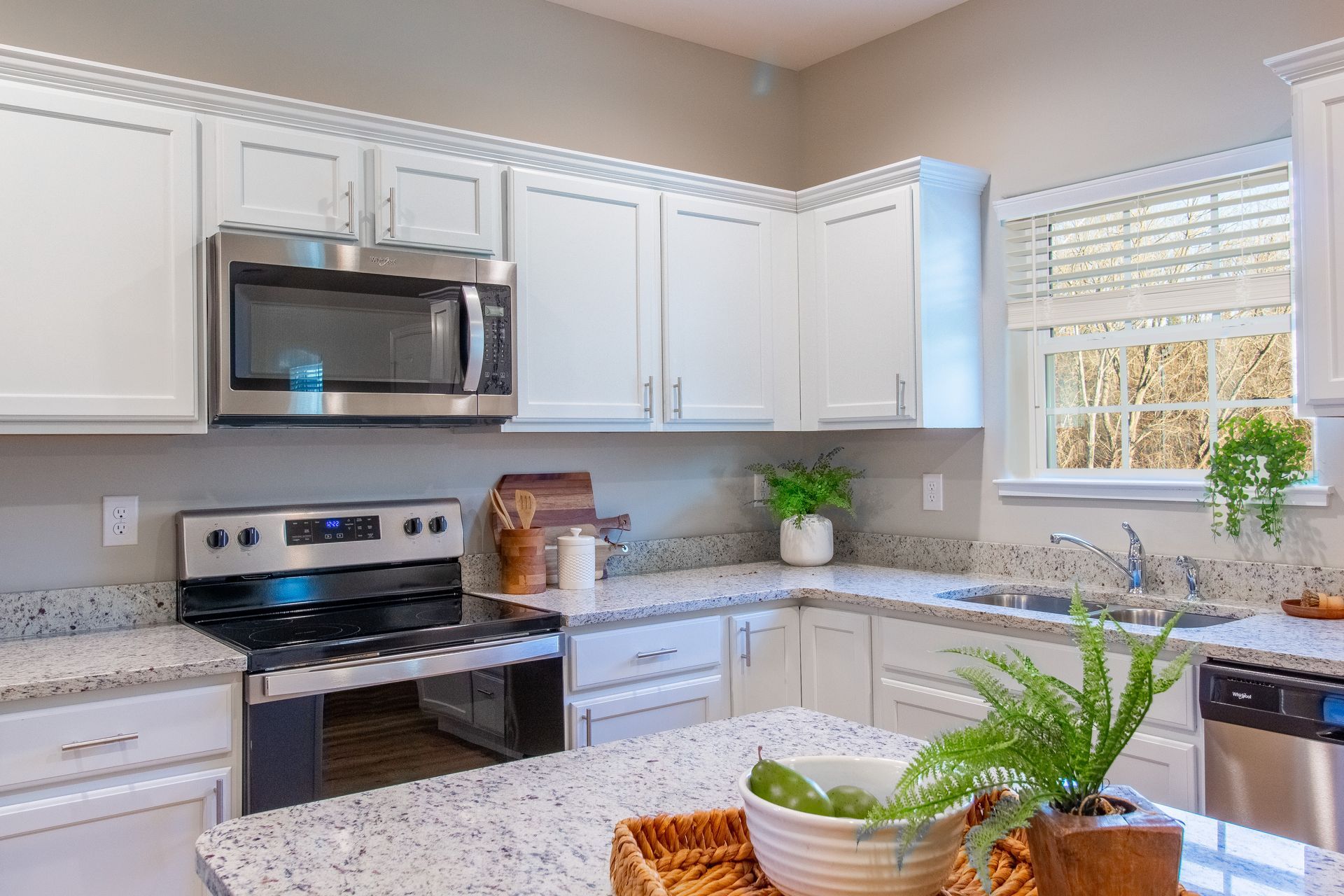 Bright modern kitchen with white cabinets, stainless appliances, granite counters, and a sunlit window