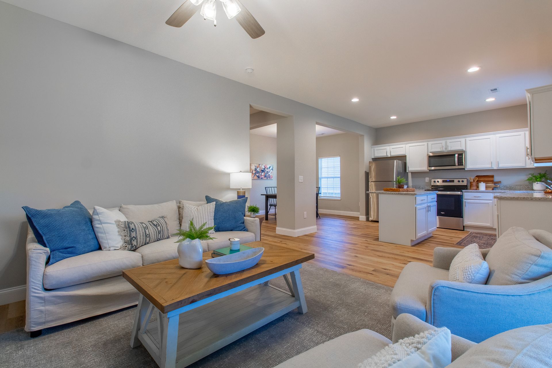 Bright open living room and kitchen with gray sofa, blue accents, and wooden coffee table