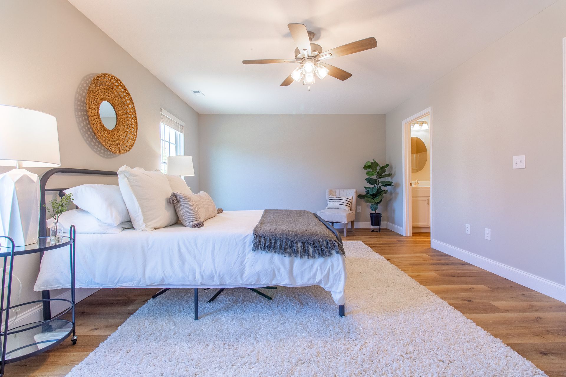 Bright bedroom with white bedding, wood floor, ceiling fan, and a small desk by the window.