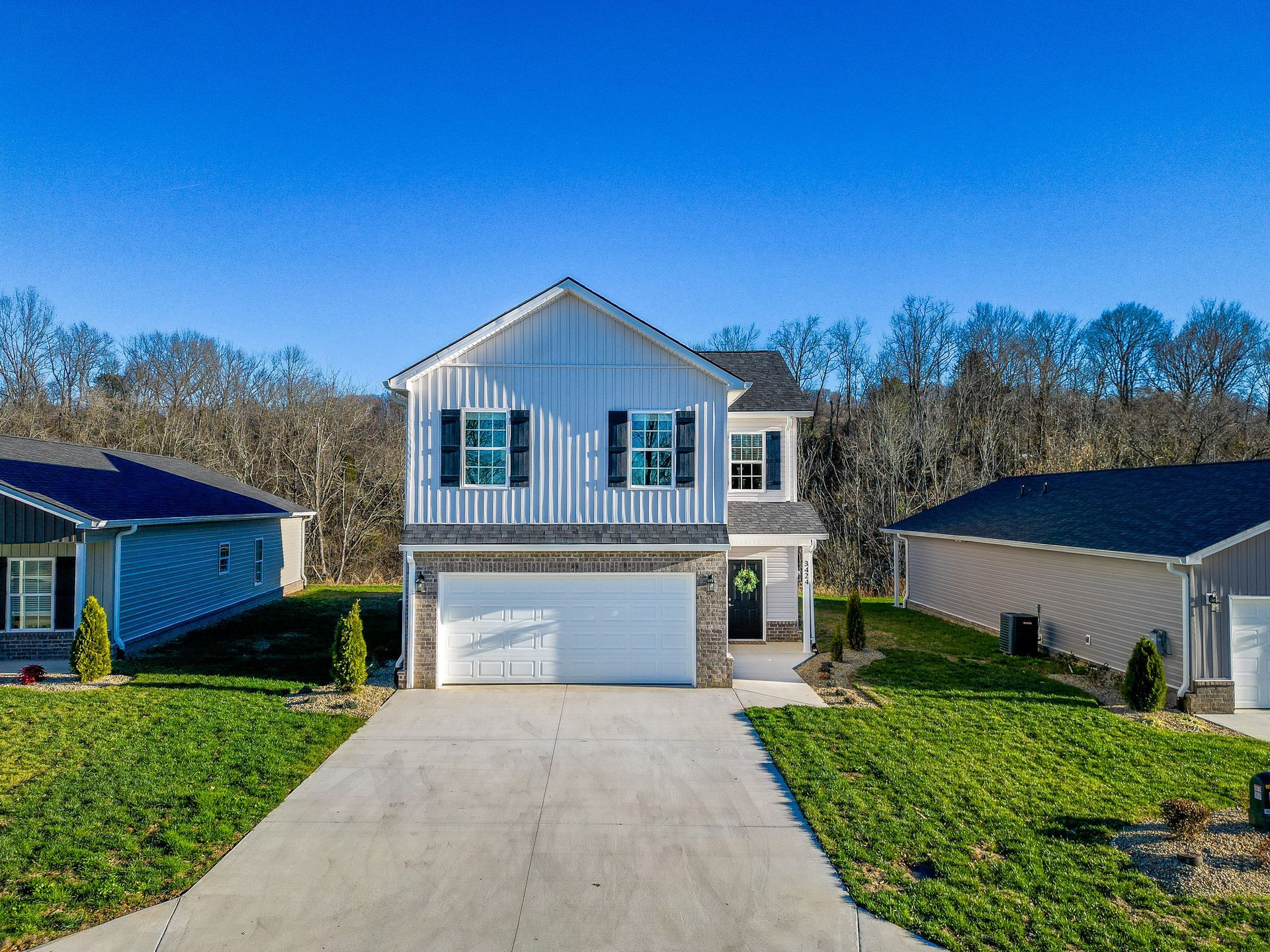 Two-story white house with a garage and long driveway under a clear blue sky
