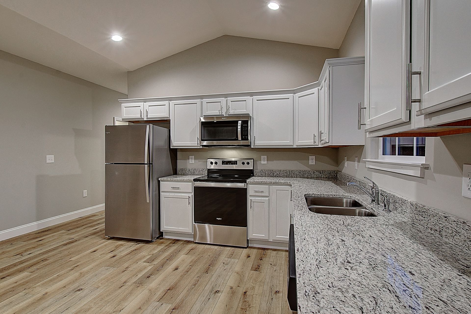 Bright modern kitchen with stainless appliances, white cabinets, and granite countertops.