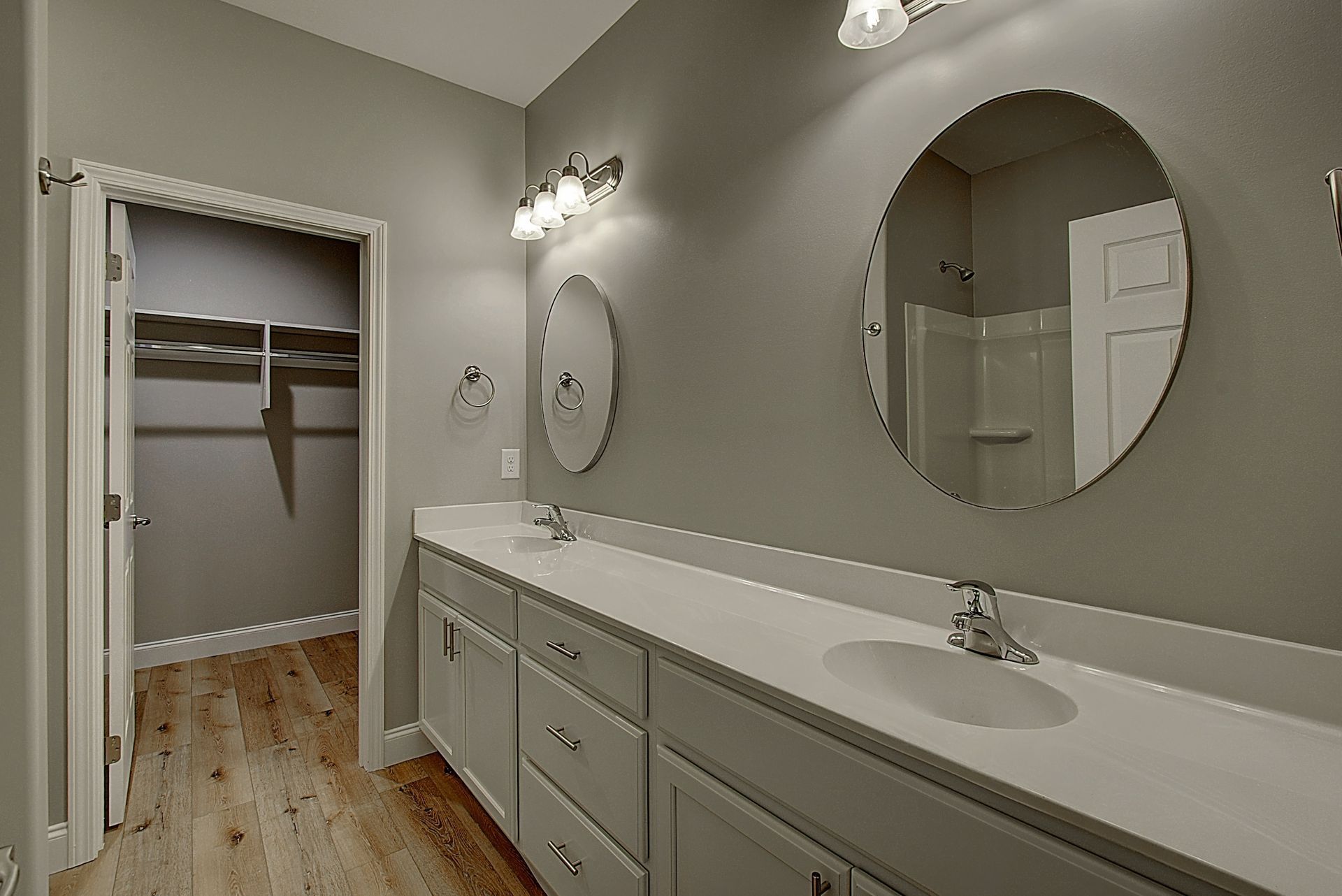 Long bathroom vanity with double sink, large mirror, and open walk-in closet in the background.