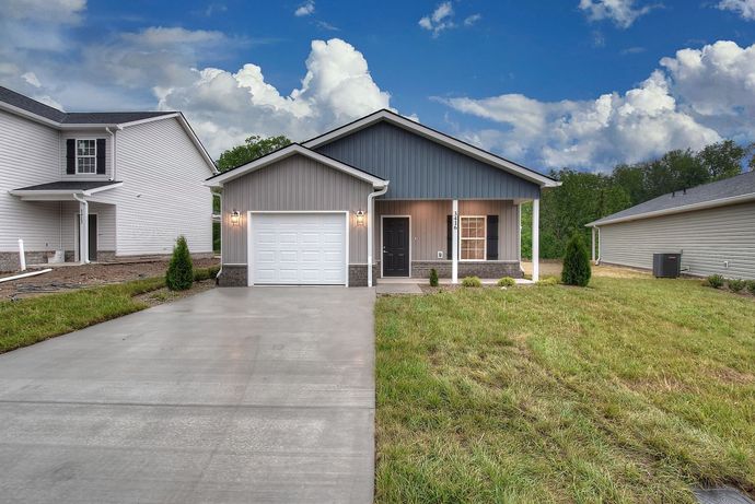 Modern single-story house with gray siding, attached garage, driveway, and a grassy front yard under a blue sky