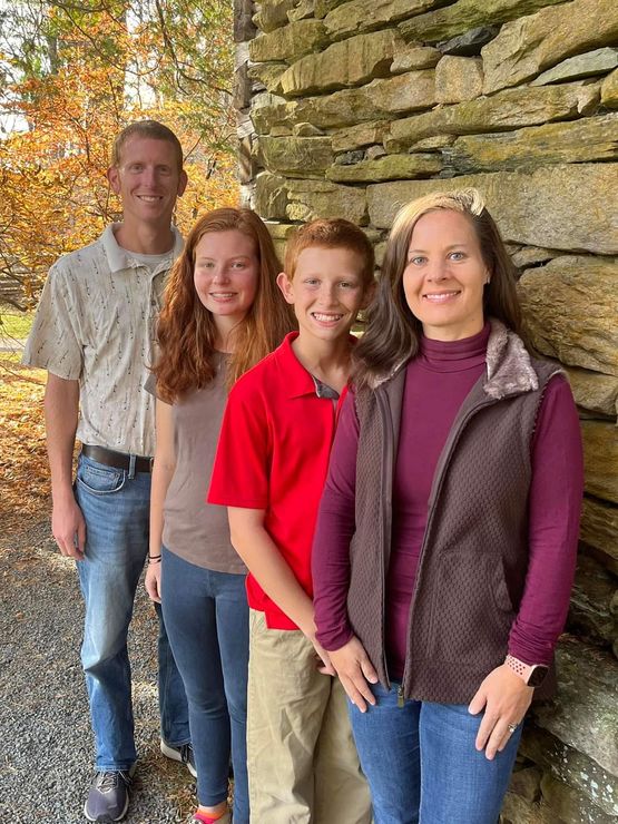 A family is posing for a picture in front of a stone wall.