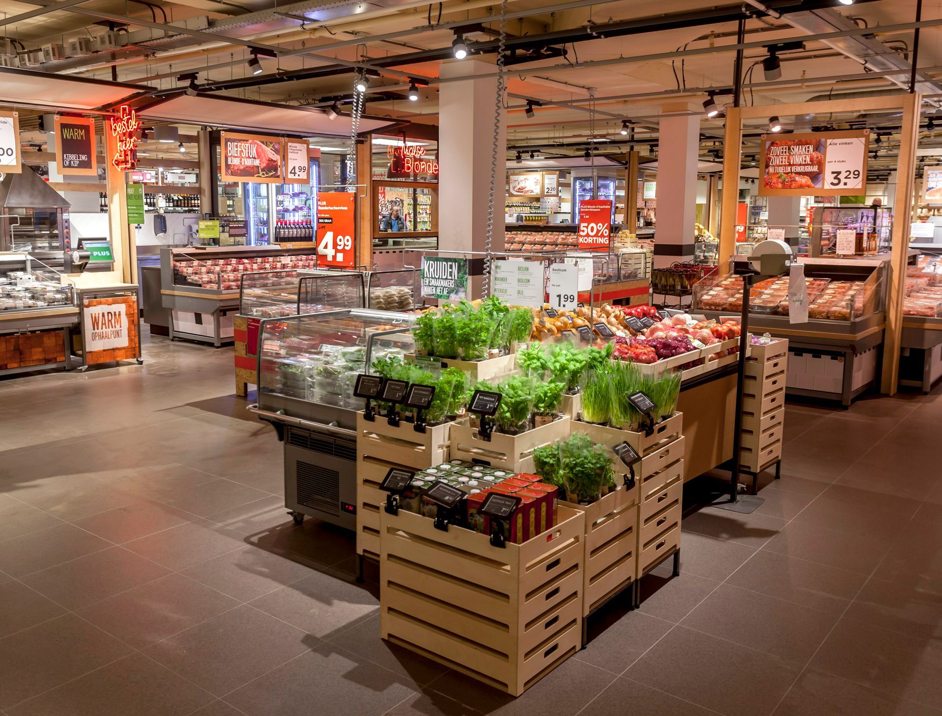 De groente- en fruitafdeling in een supermarkt met houten kratten vol verse groenten en fruit onder warme verlichting.