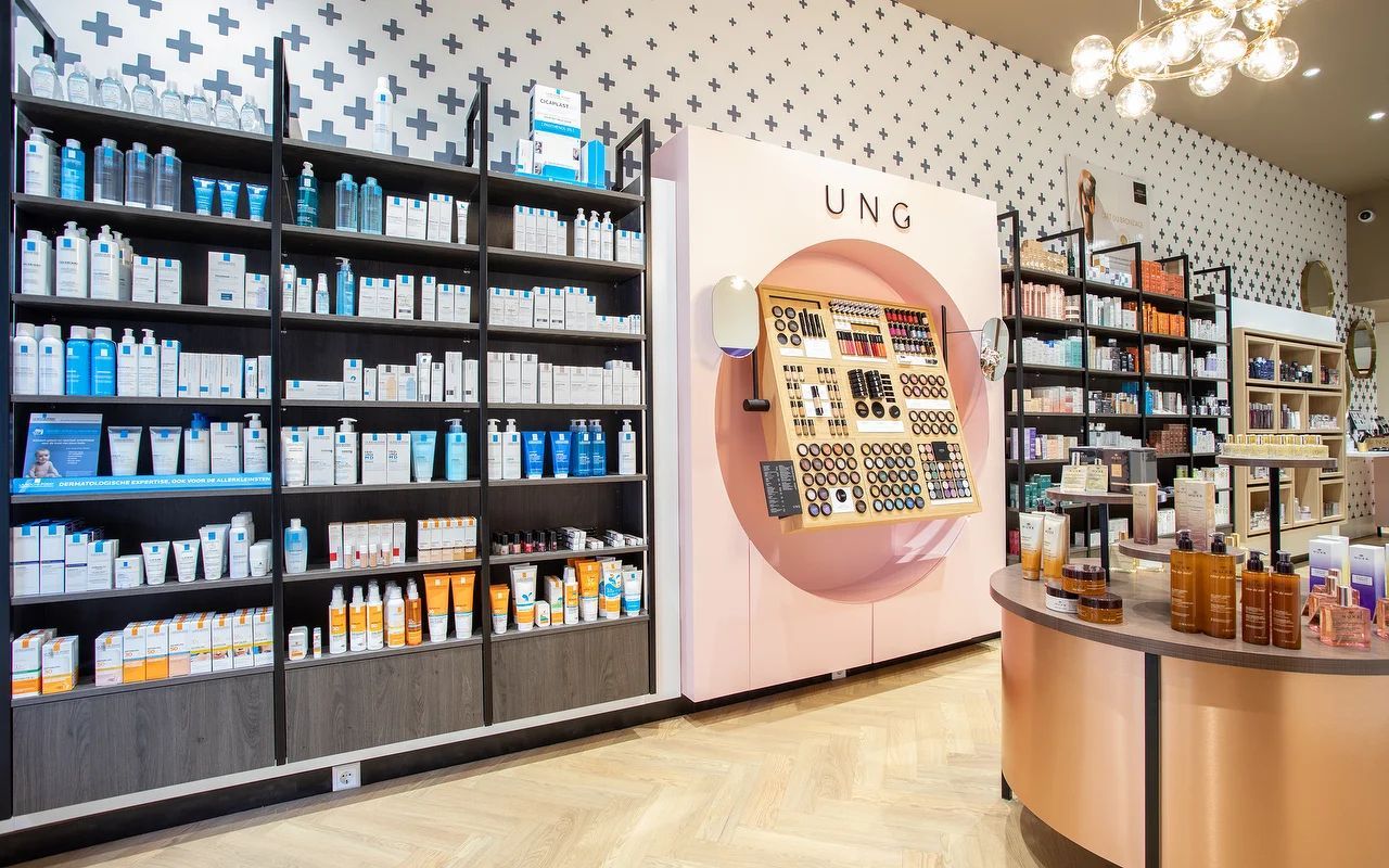 Schappen vol schoonheidsproducten in een lichte, moderne winkel met een ronde display en een koperen toonbank.