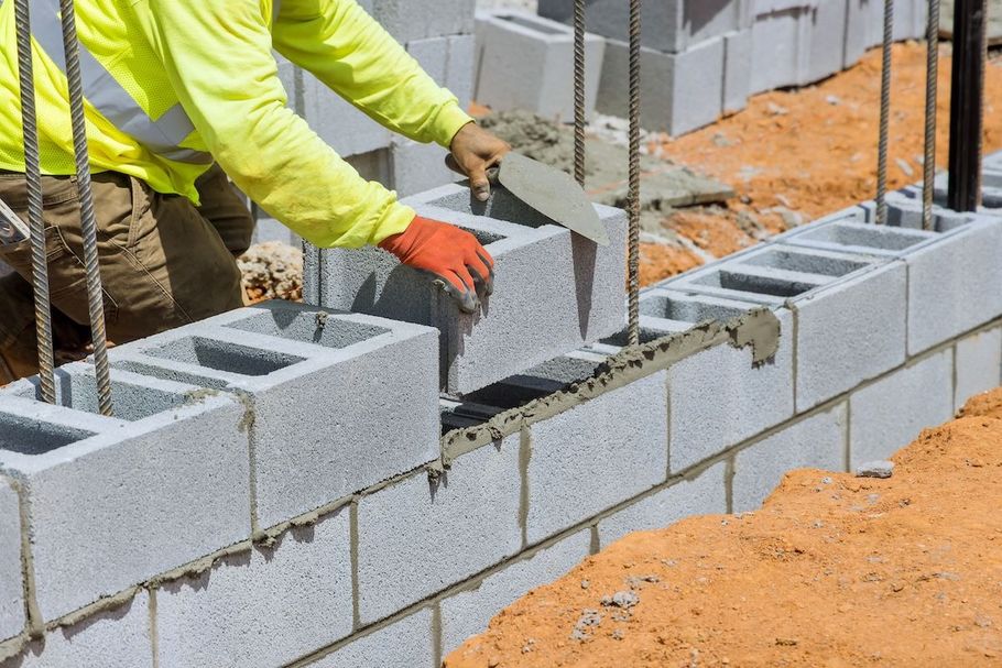 Construction worker laying cinder blocks on a wall with a trowel at a building site
